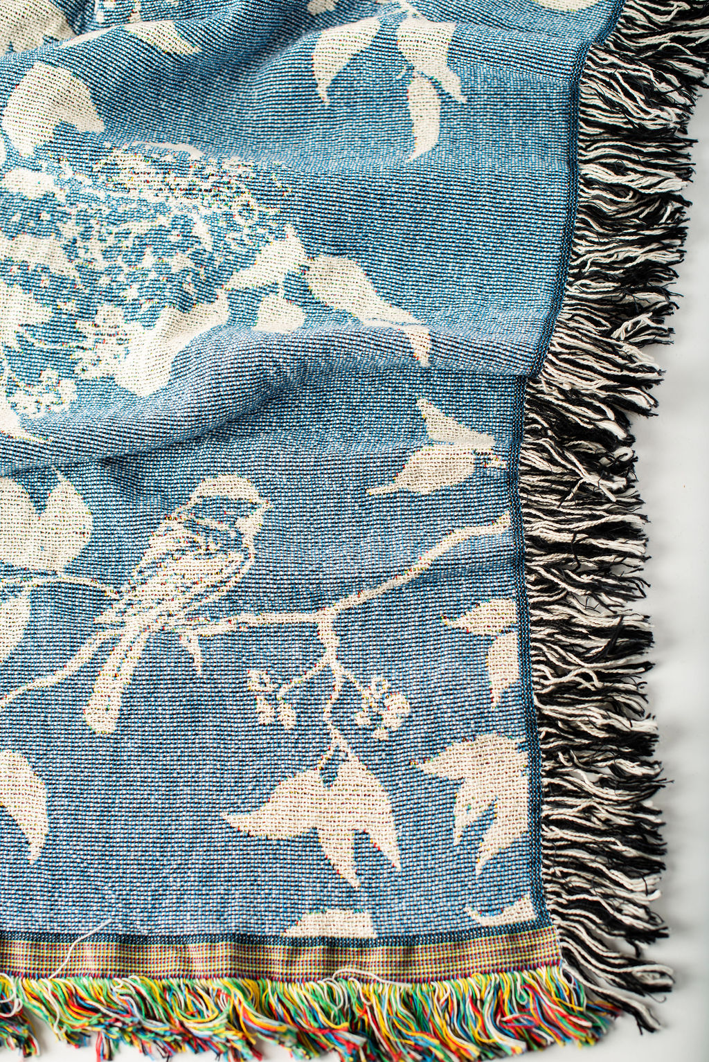 Close-up of Wren Chambray blue and cream bird and botanical woven cotton throw with fringe