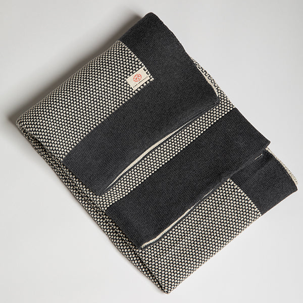 Folded dark grey and white textured cotton throw with a dark grey border and a Pink Lemonade brand label stitched on it. 