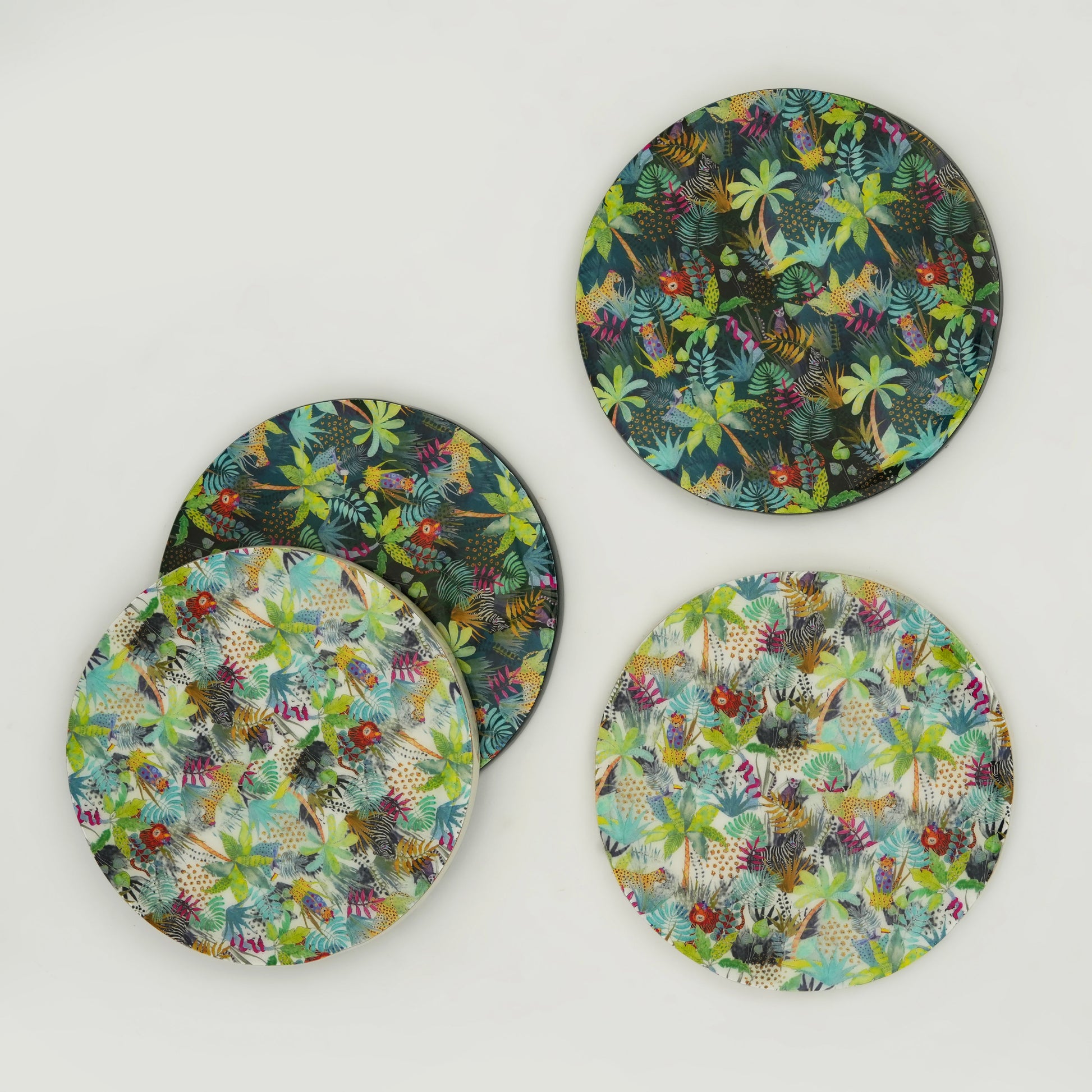 Overhead view of four round MDF coasters with a colorful jungle-inspired leaf and flower pattern.