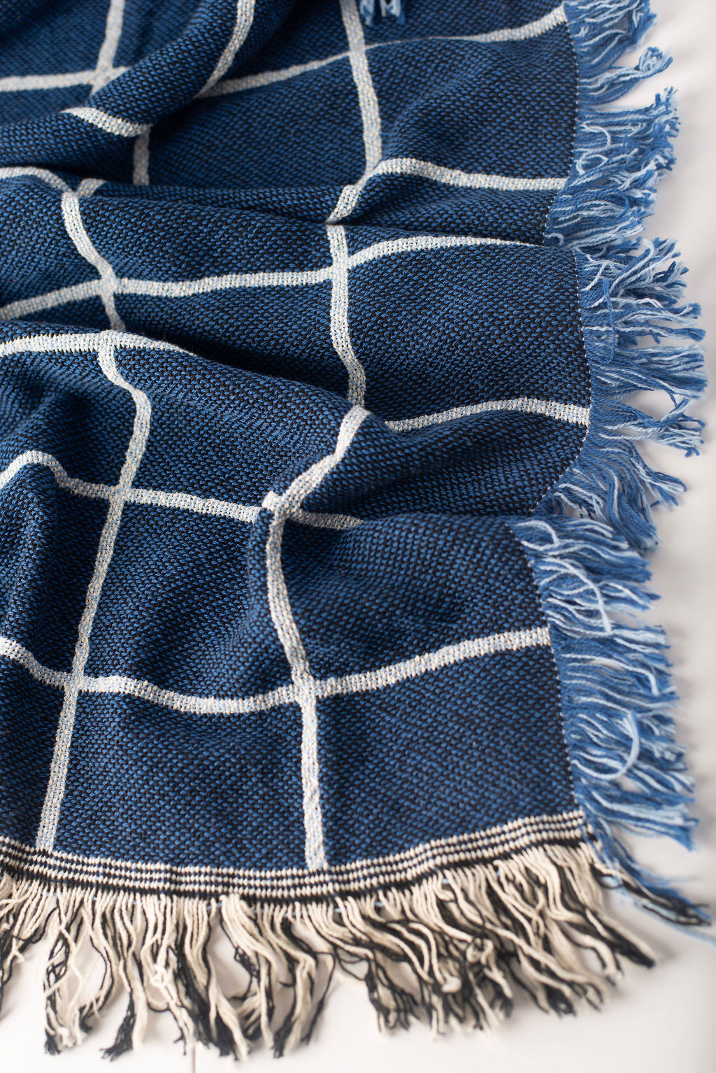 Greer Lapis blue grid woven throw displayed on a wooden dresser with gold and charcoal Greer blankets