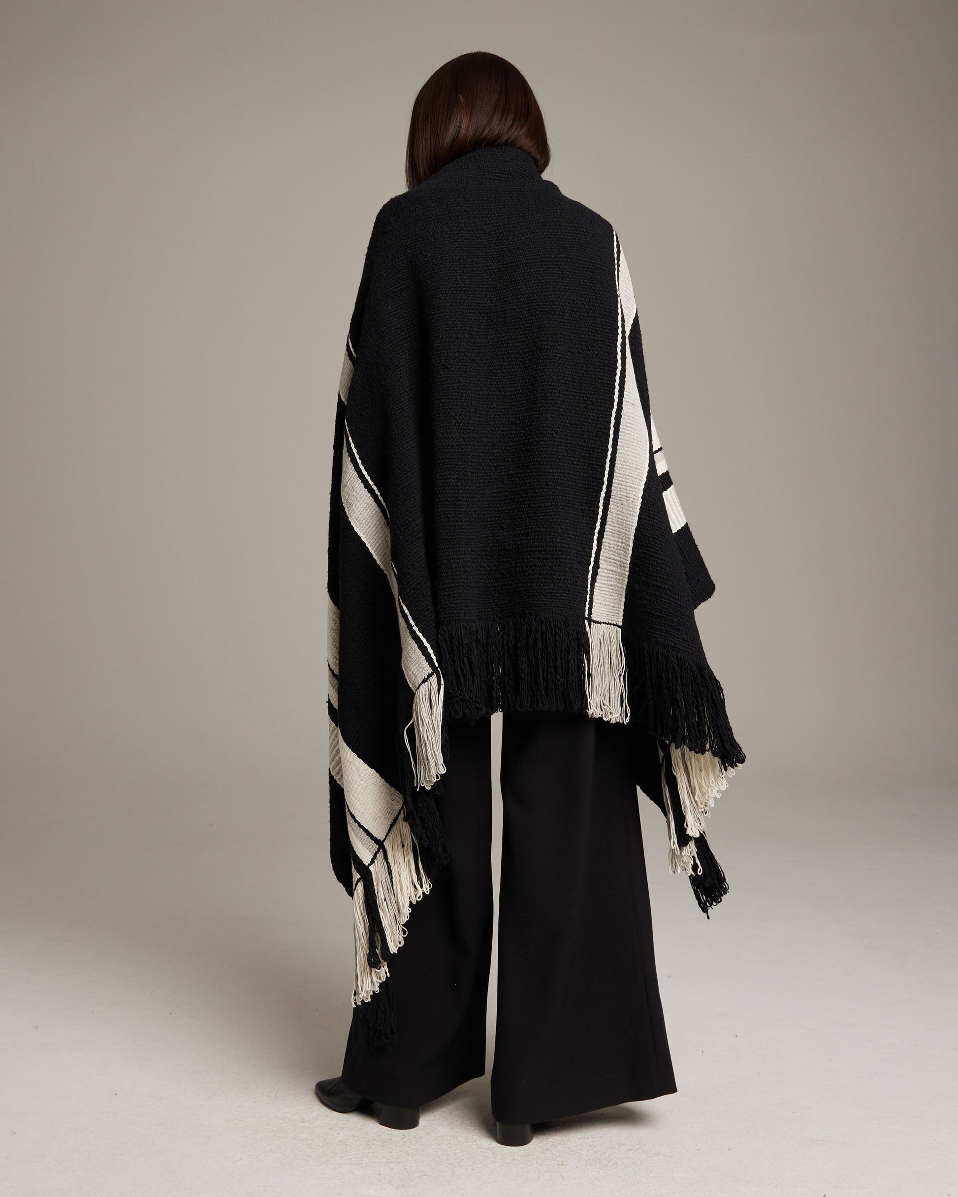Model wearing a black and white Granite Cascade Blanket with fringe, viewed from the back