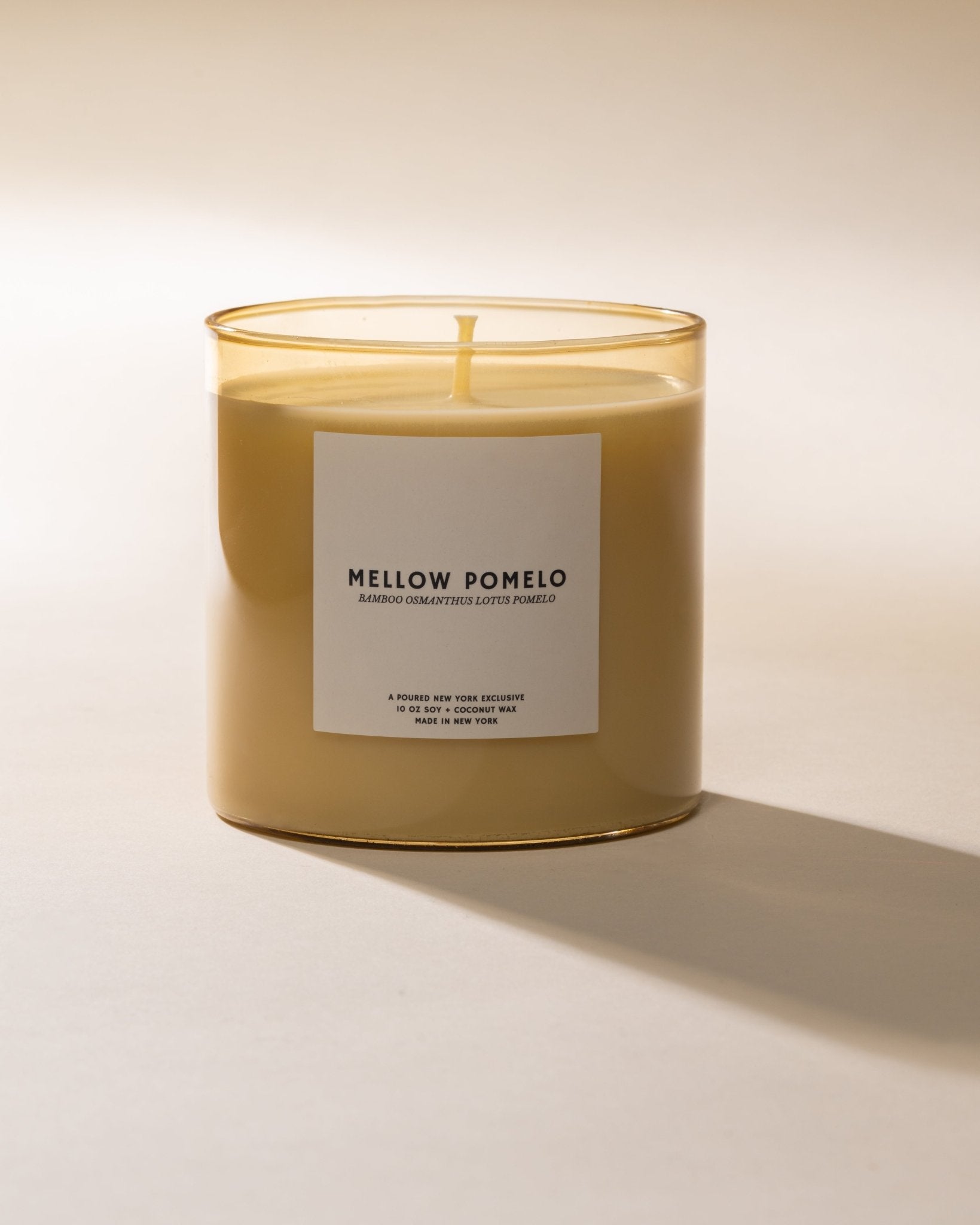 Poured New York Candle labeled 'Mellow Pomelo' in a butter yellow glass on a beige background