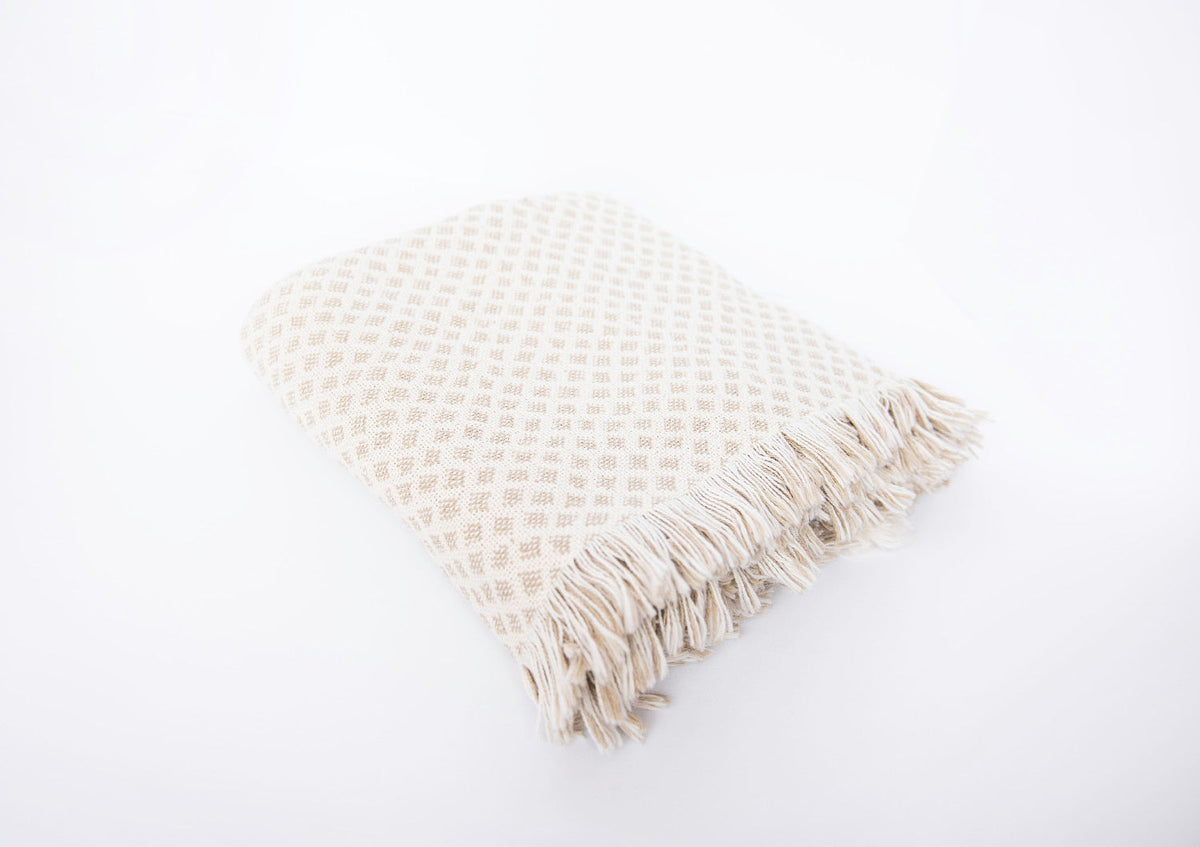 Side view of folded Rowan neutral diamond-patterned woven throw with fringe