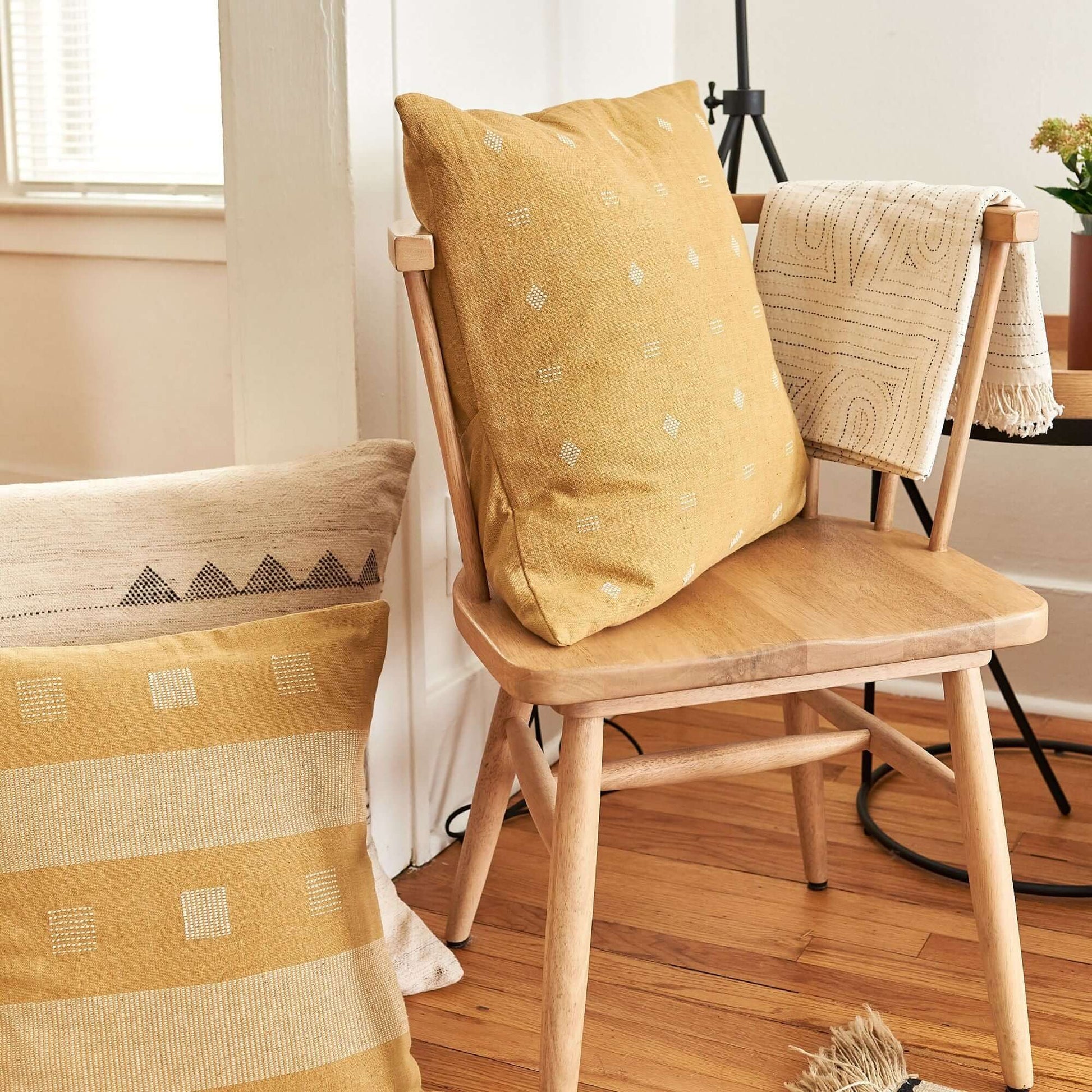 Nira Ochre Hand Spun Organic Cotton Handloom Pillow on a cozy wooden chair with textured fabric.