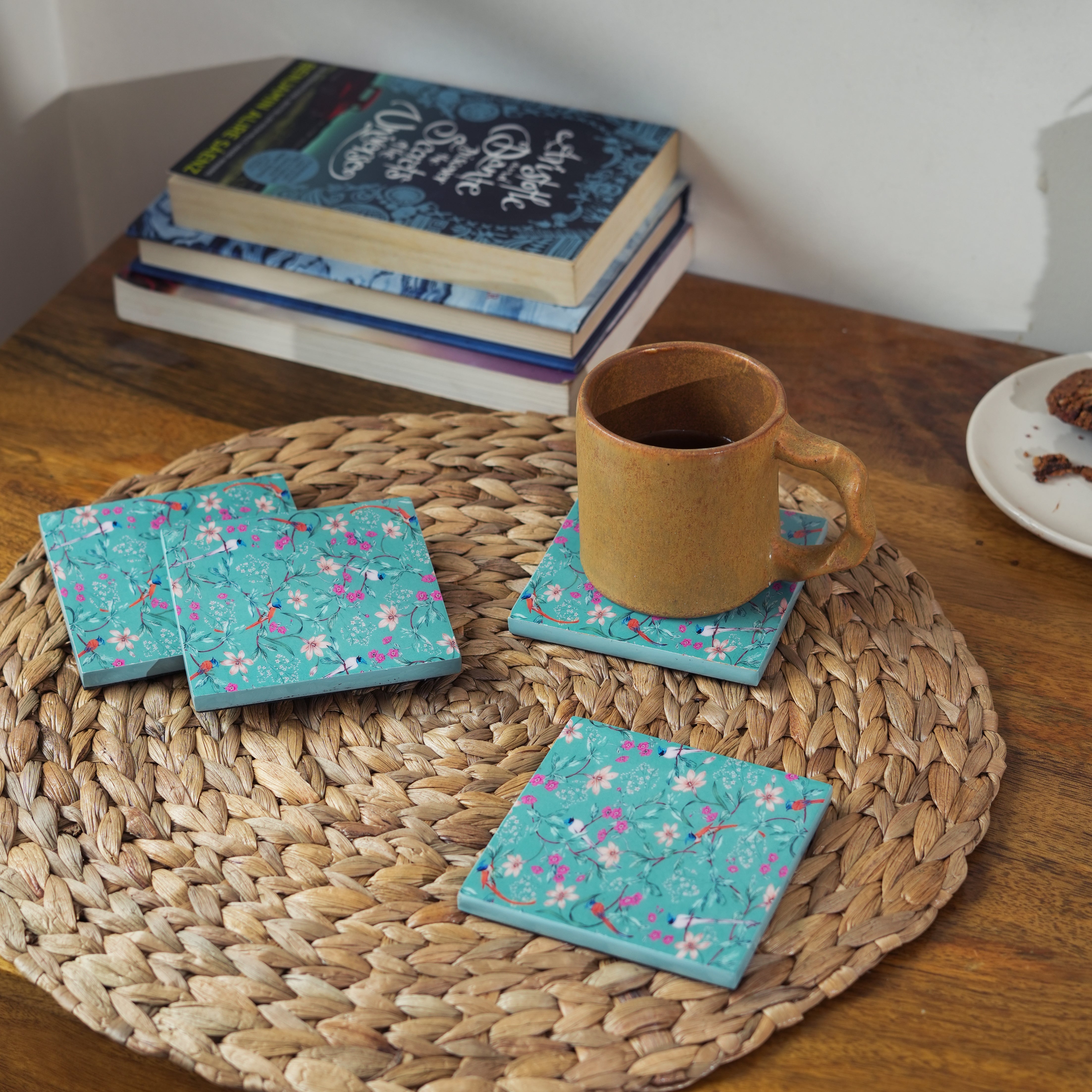 Teal floral coasters on a woven placemat with a mug and books in the background.