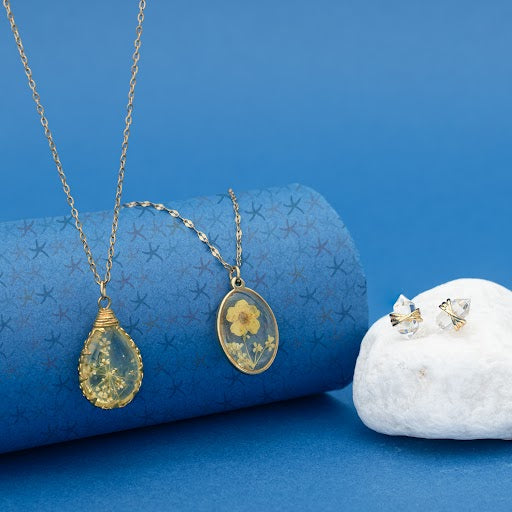 Stronger Together crystal studs with pressed flower pendant necklaces on blue