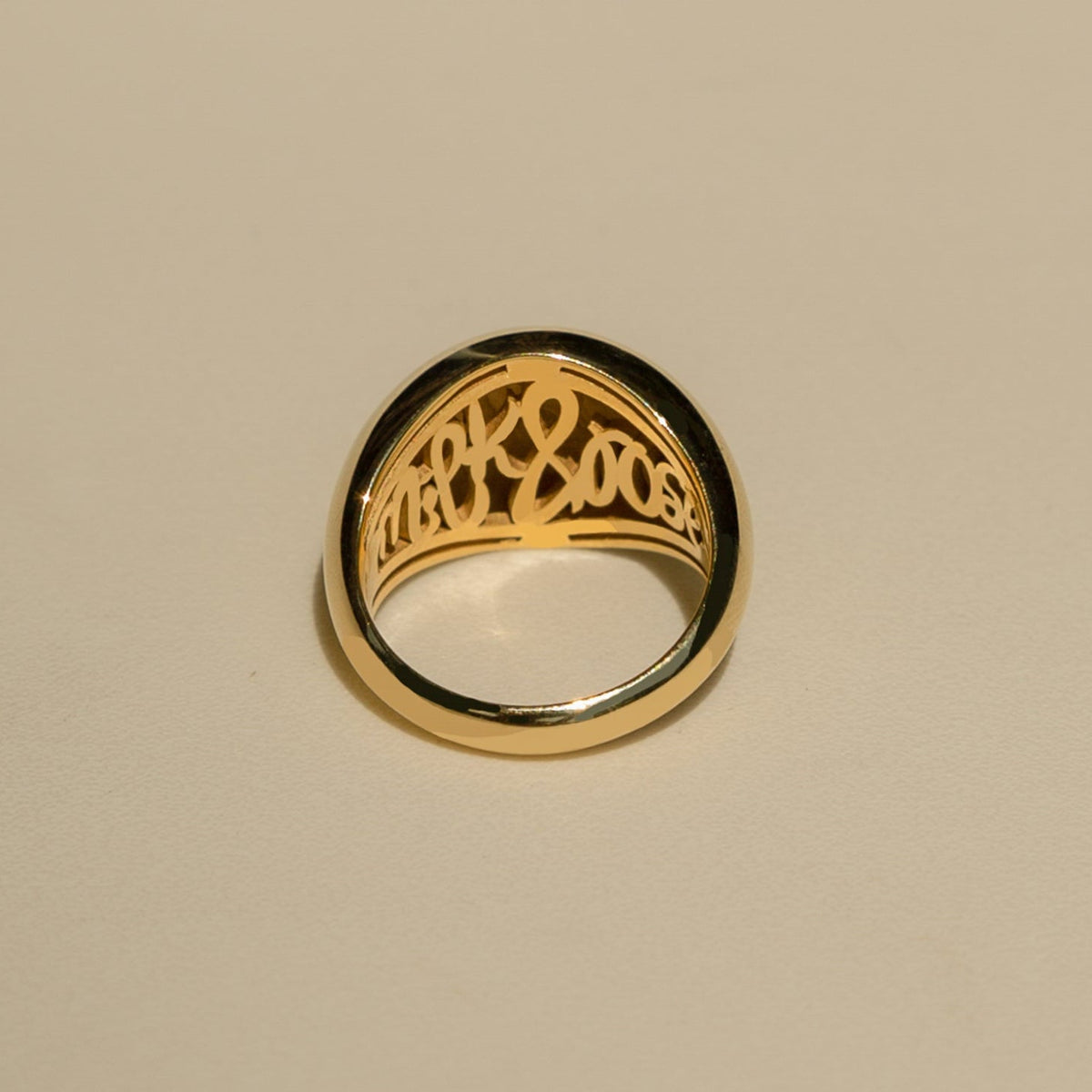 Gold ring with intricate design on a beige background