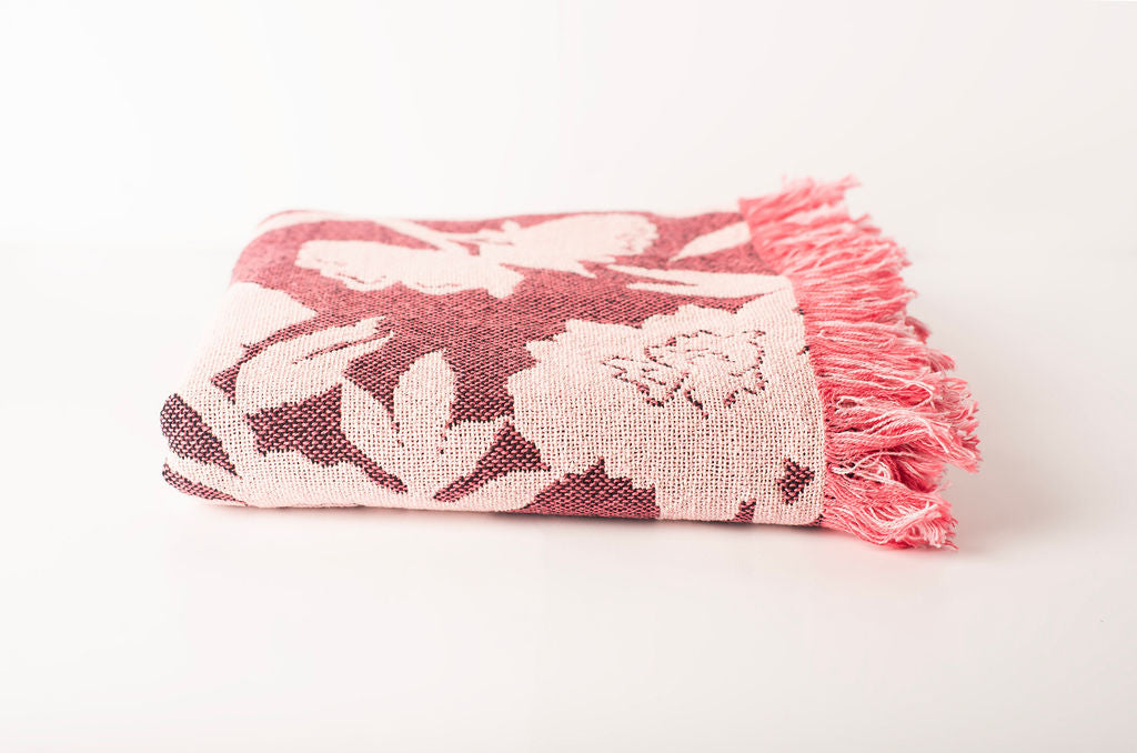 Front view of folded mulberry pink and cream floral woven cotton throw on a white background