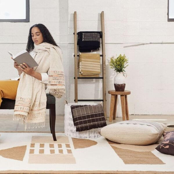 Unah Coral Fully Hand Embroidered Handwoven Organic Cotton Throw used by a woman reading in a cozy living room setting.