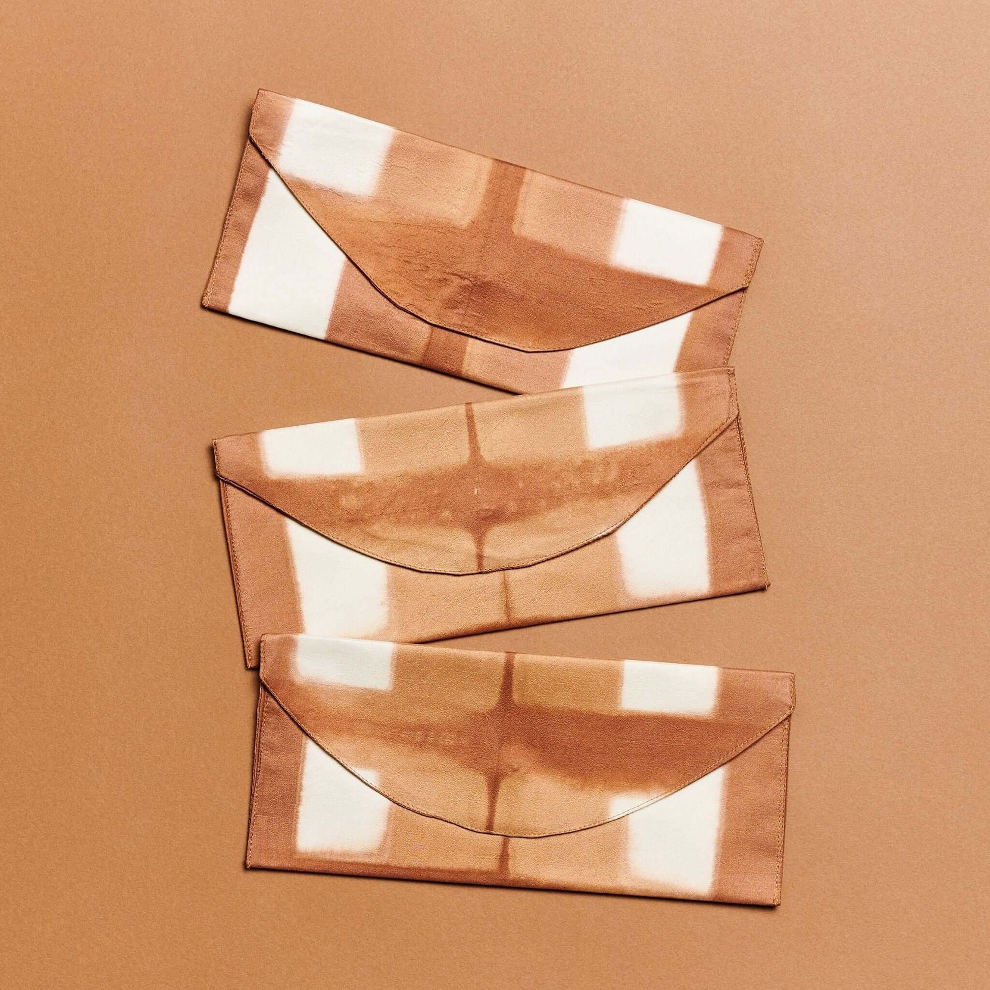 Melo Gold Mulberry Silk Shibori Hand Crafted Envelope Pouch showcasing three unique designs on a warm background.
