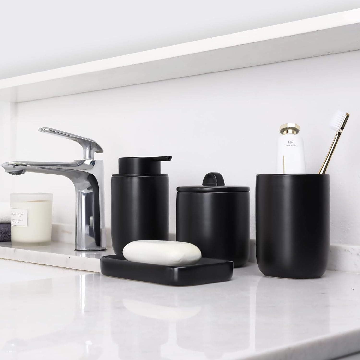 A set of black ceramic bathroom accessories including a foaming soap dispenser, a toothbrush holder, a Qtip holder, and a cotton ball holder, displayed on a marble countertop.