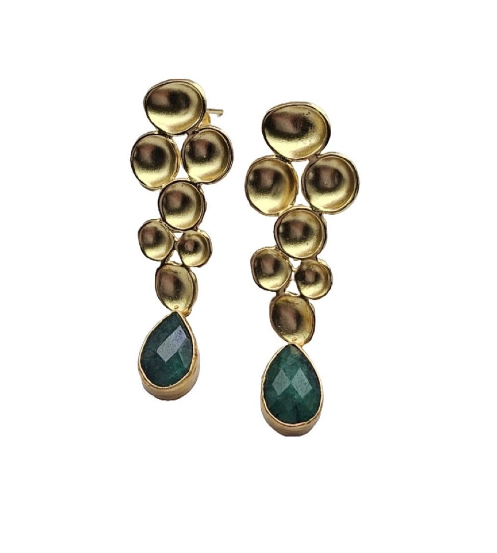 A pair of gold drop earrings featuring  geometric gold metal design and a faceted green teardrop emerald gemstone at the bottom, set against a plain white background.