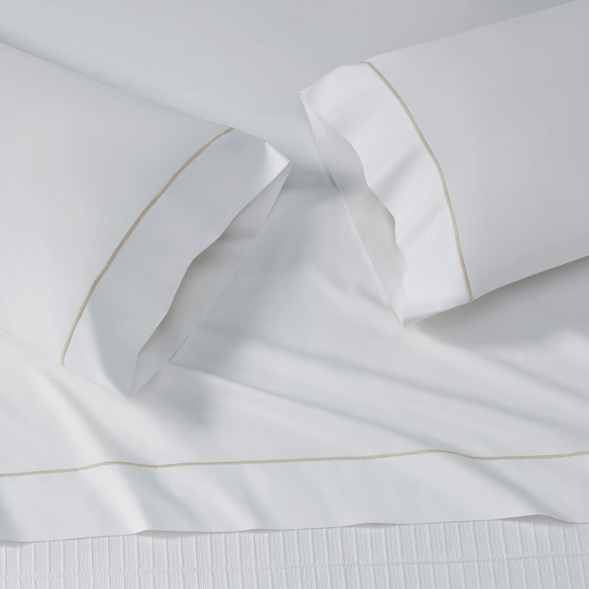 ASP-531-2032_3|White 100% cotton flat sheet and two matching pillowcases on a bed, all featuring subtle tan piped borders.