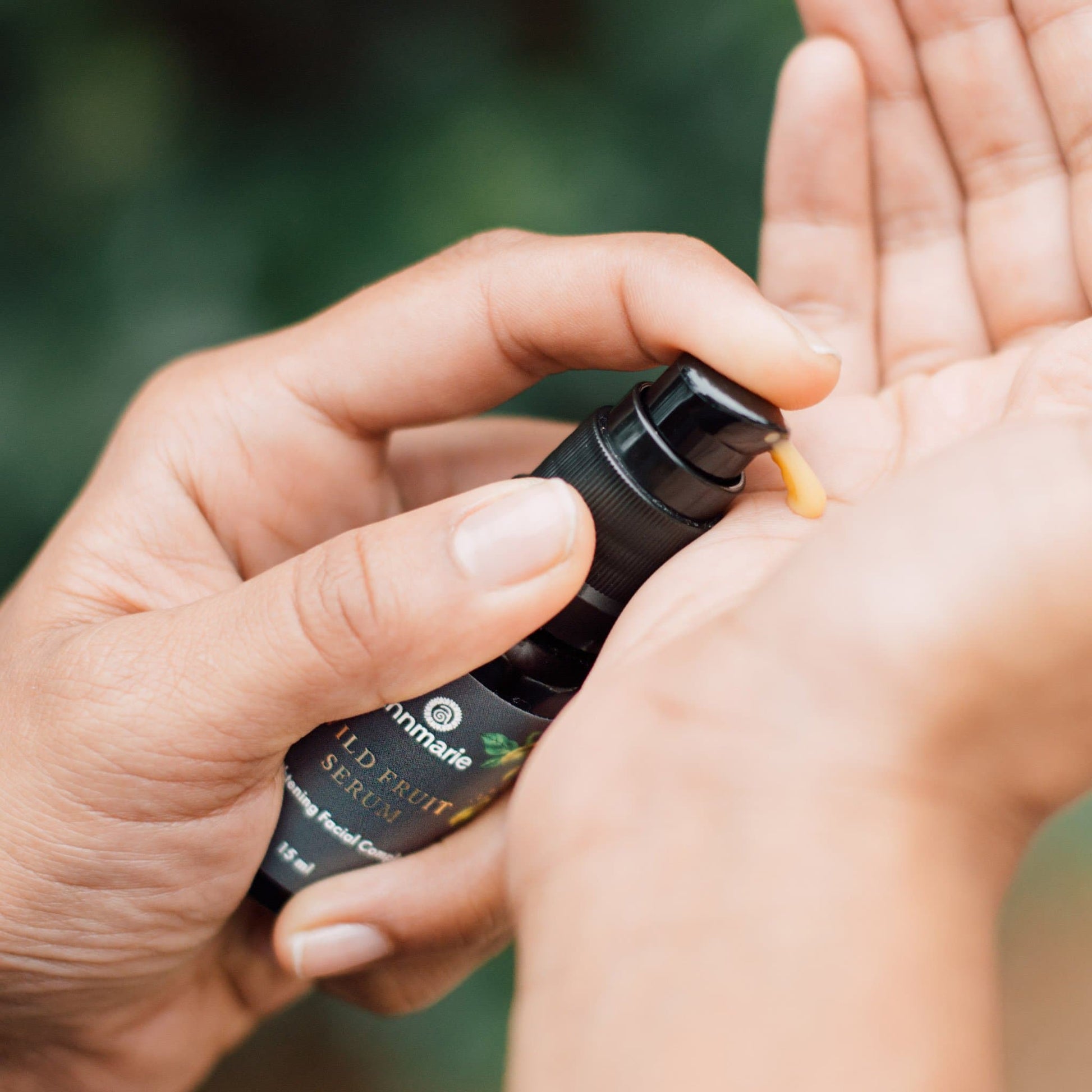 Hand dispensing Annmarie Wild Fruit Serum from a pump bottle onto palm before applying to skin.