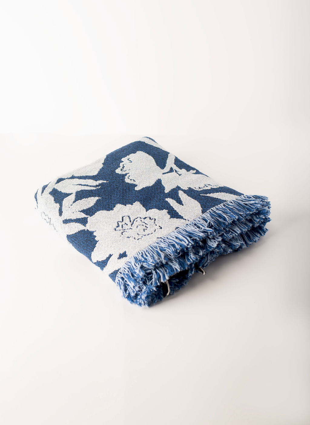 Close-up corner view ow blue and light blue patterned blanket with fringe on a light background