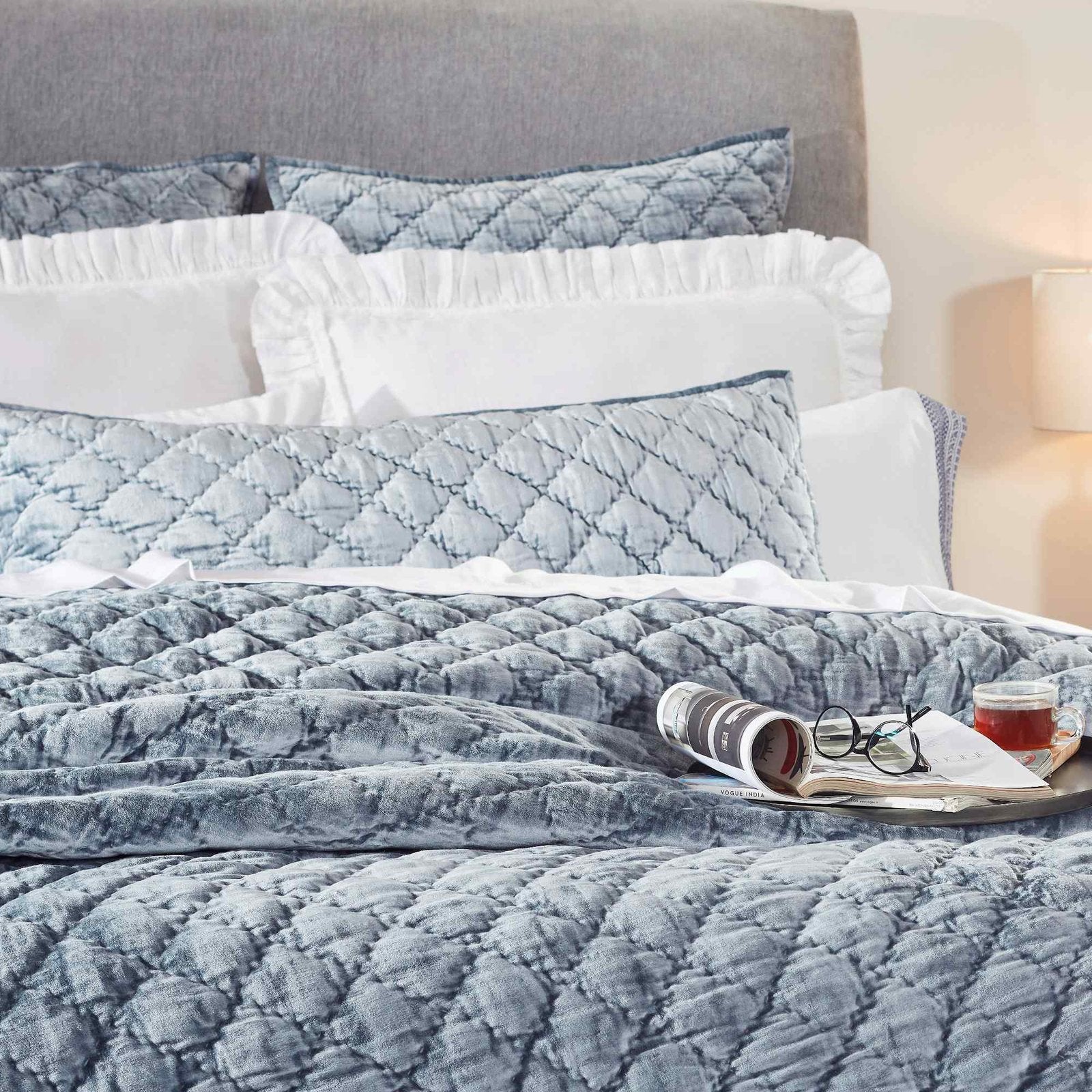 QT-341-9496_2|Close-up of luxurious blue velvet diamond-quilted quilt on a bed, with magazine and tea. Cozy, elegant bedroom.