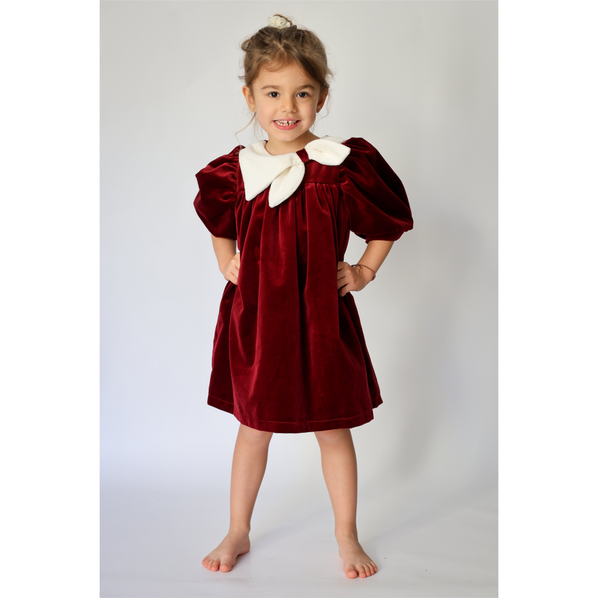 Young girl wearing a burgundy velvet dress with white collar against a plain background