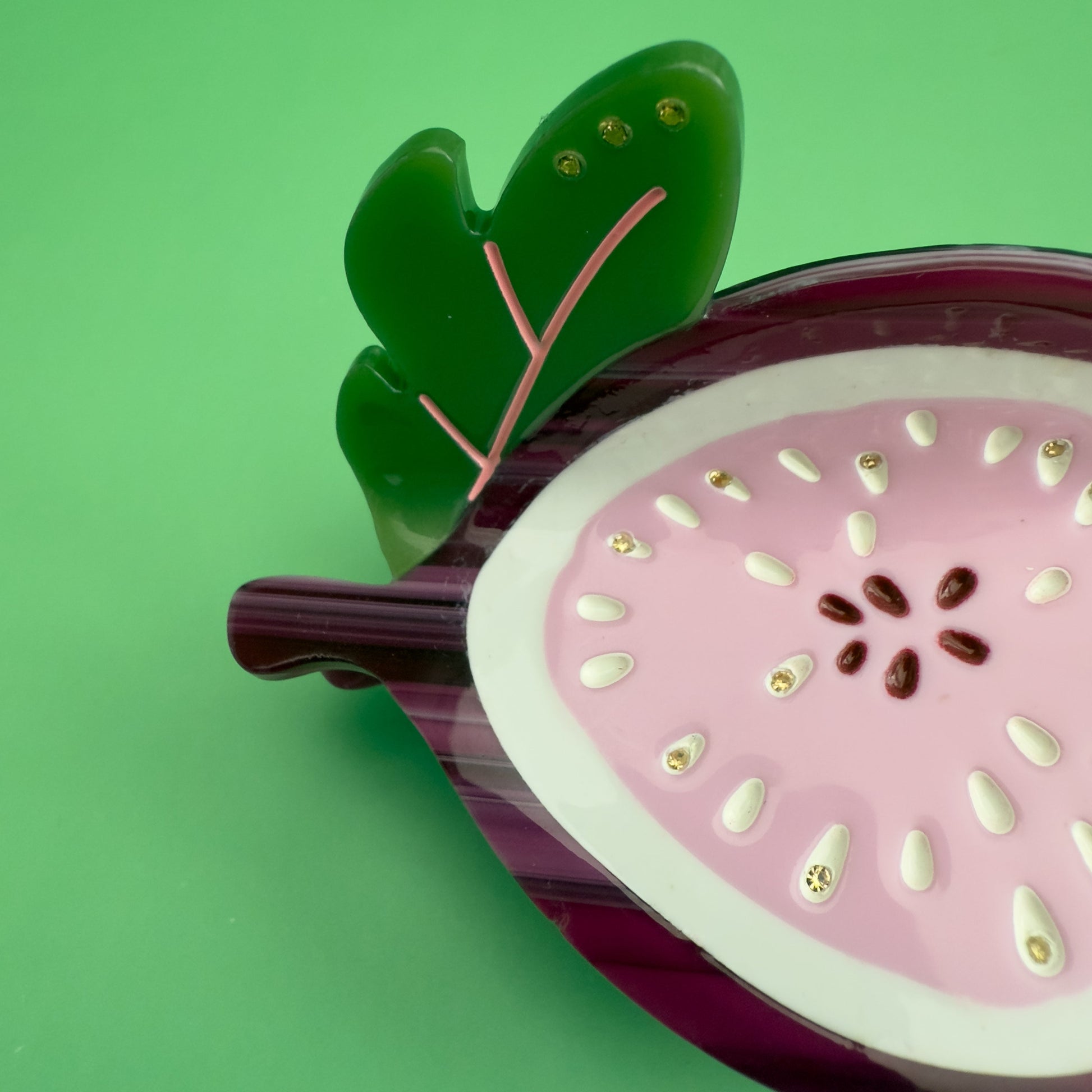 Decorative hair claw like a sliced fig on a green background. 