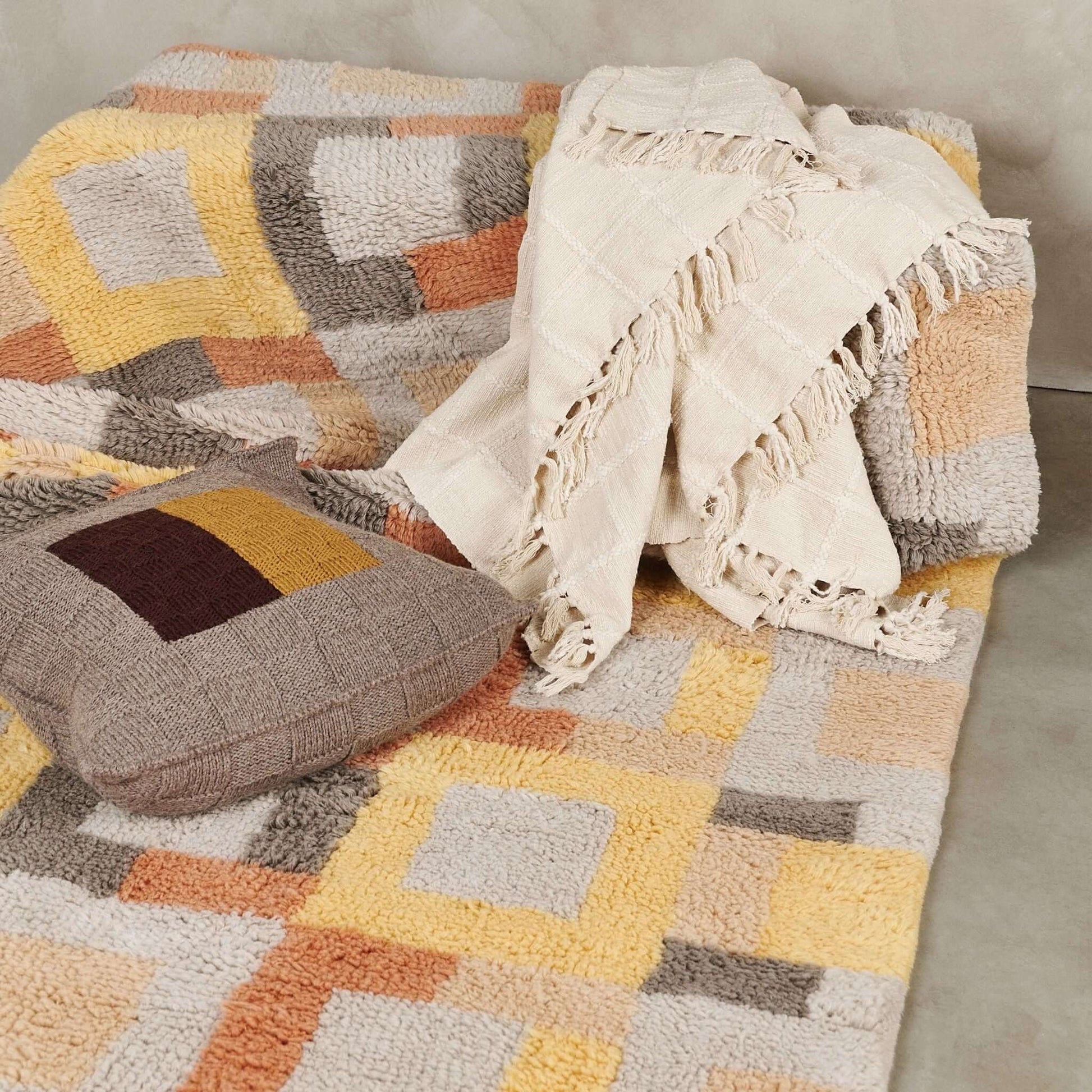 Sea Shell White Textured Checks Handloom Throw draped over a colorful geometric patterned sofa with a matching cushion.