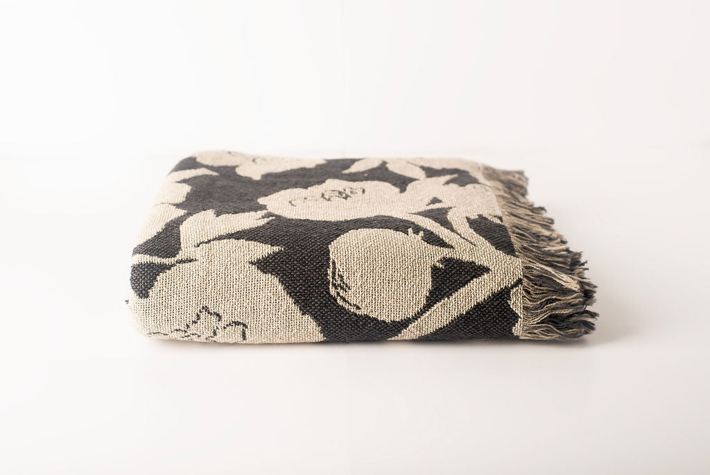 Front view of folded charcoal and cream floral woven cotton throw on a white background