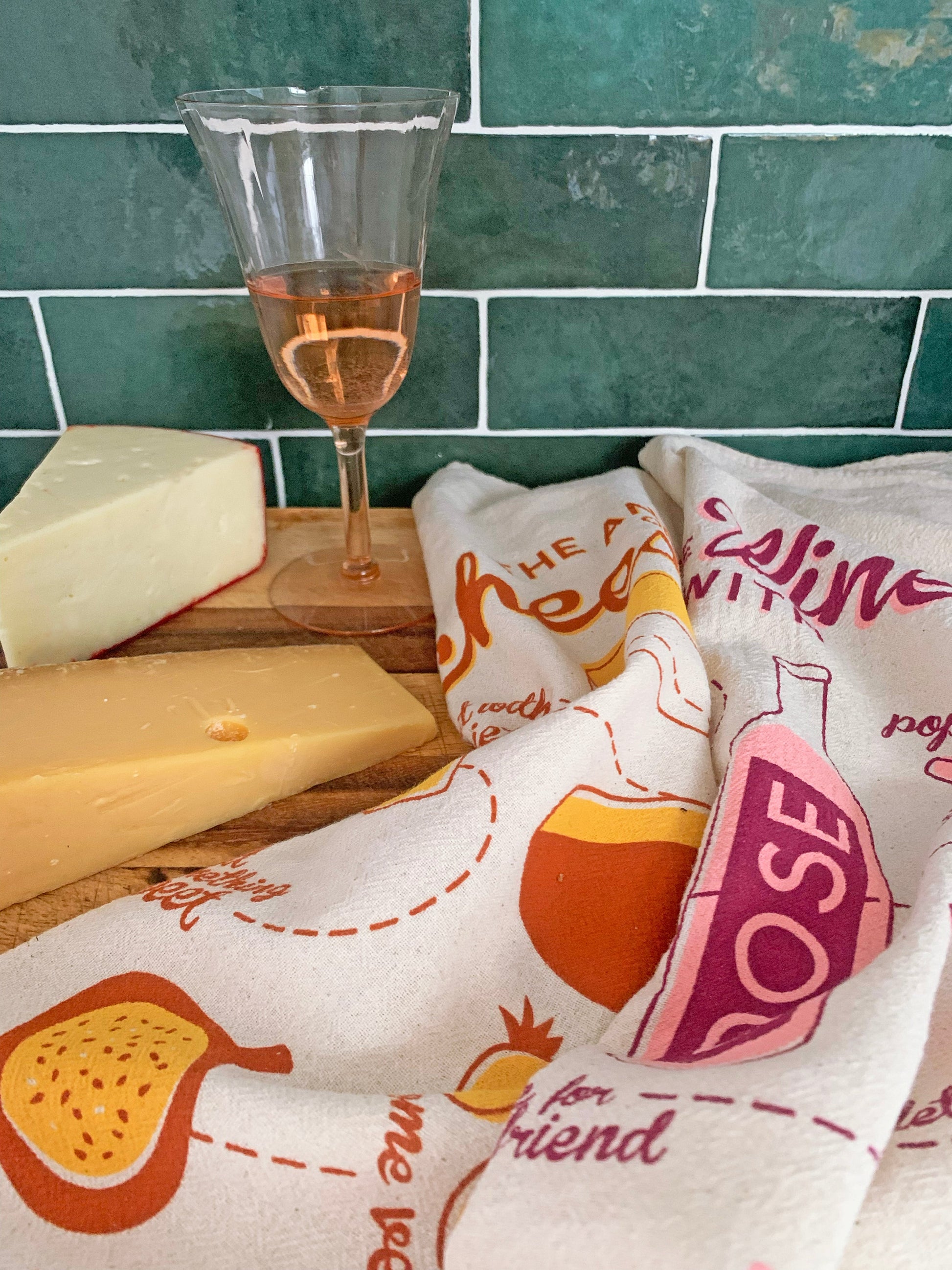 Cheese and wine dish towels photographed with cheese wedges and a glass of wine