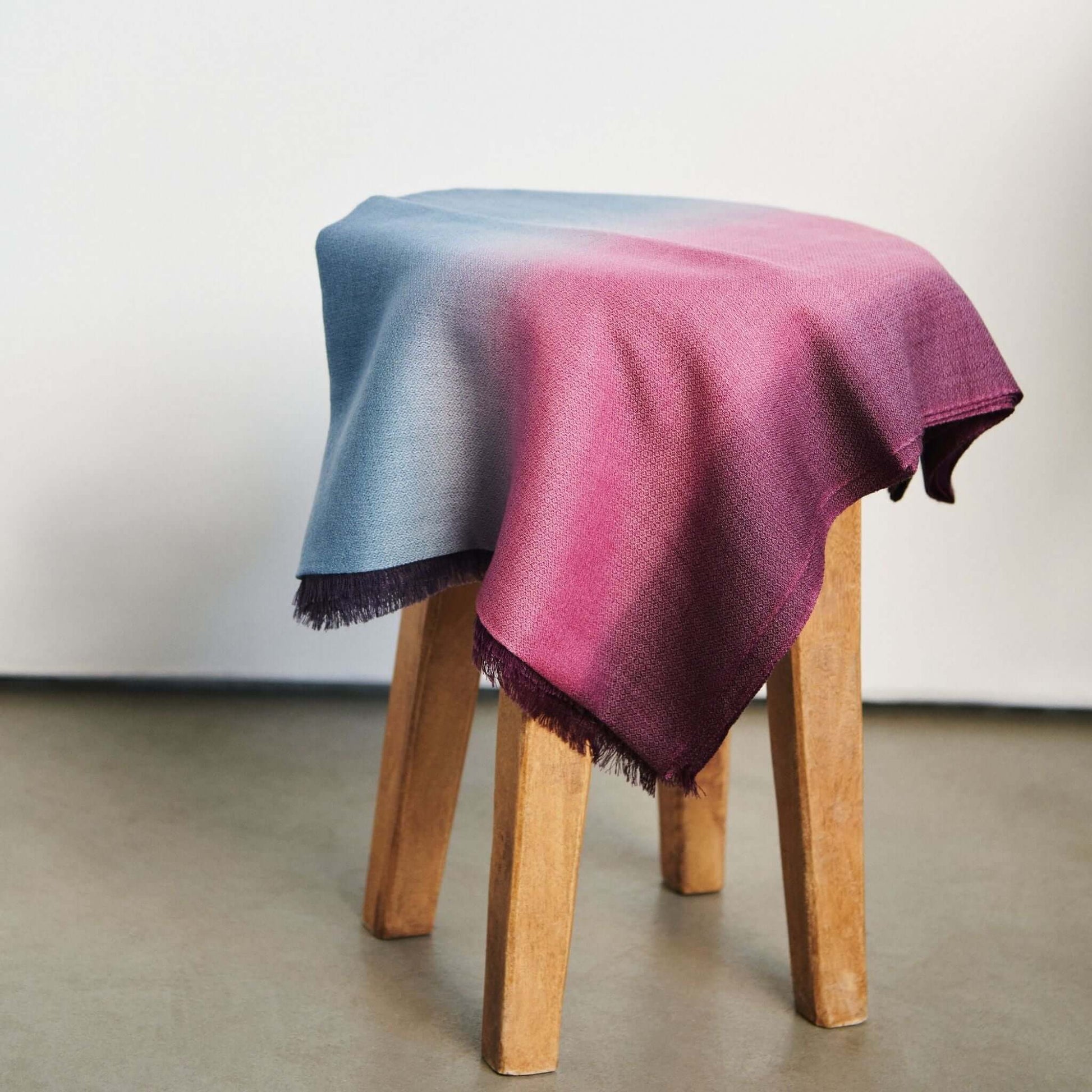 Iris Haze Blue Pink Cashmere Merino Handloom Scarf displayed on a wooden stool with soft color gradients.