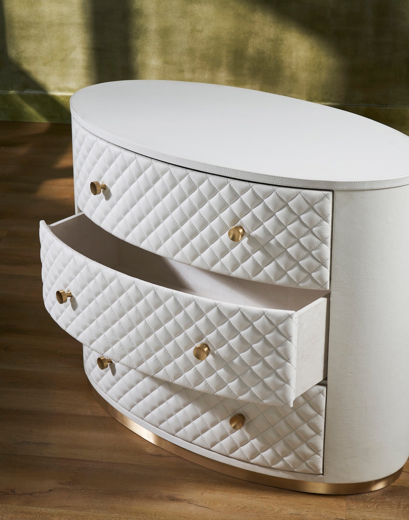 FN-5218-482036_4|Elegant white leather oval chest of drawers, featuring a chic quilted design, radiant gold hardware, and a sleek gold base.