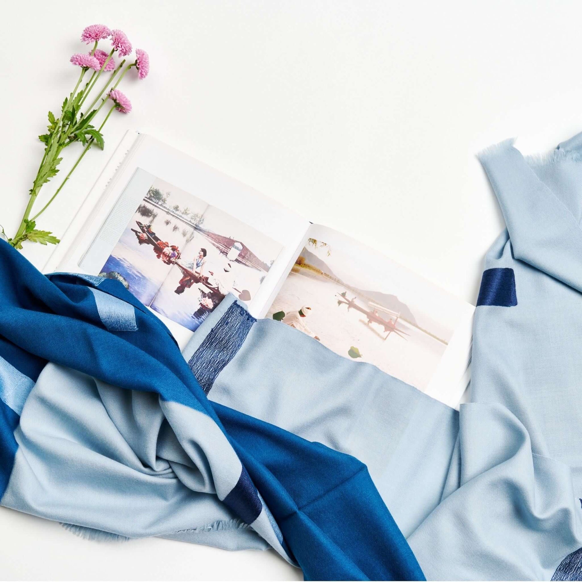 Harbor Blue Silk Merino Hand Woven Hand Embroidered Modern Artisanal Scarf displayed with a photo book and flowers.
