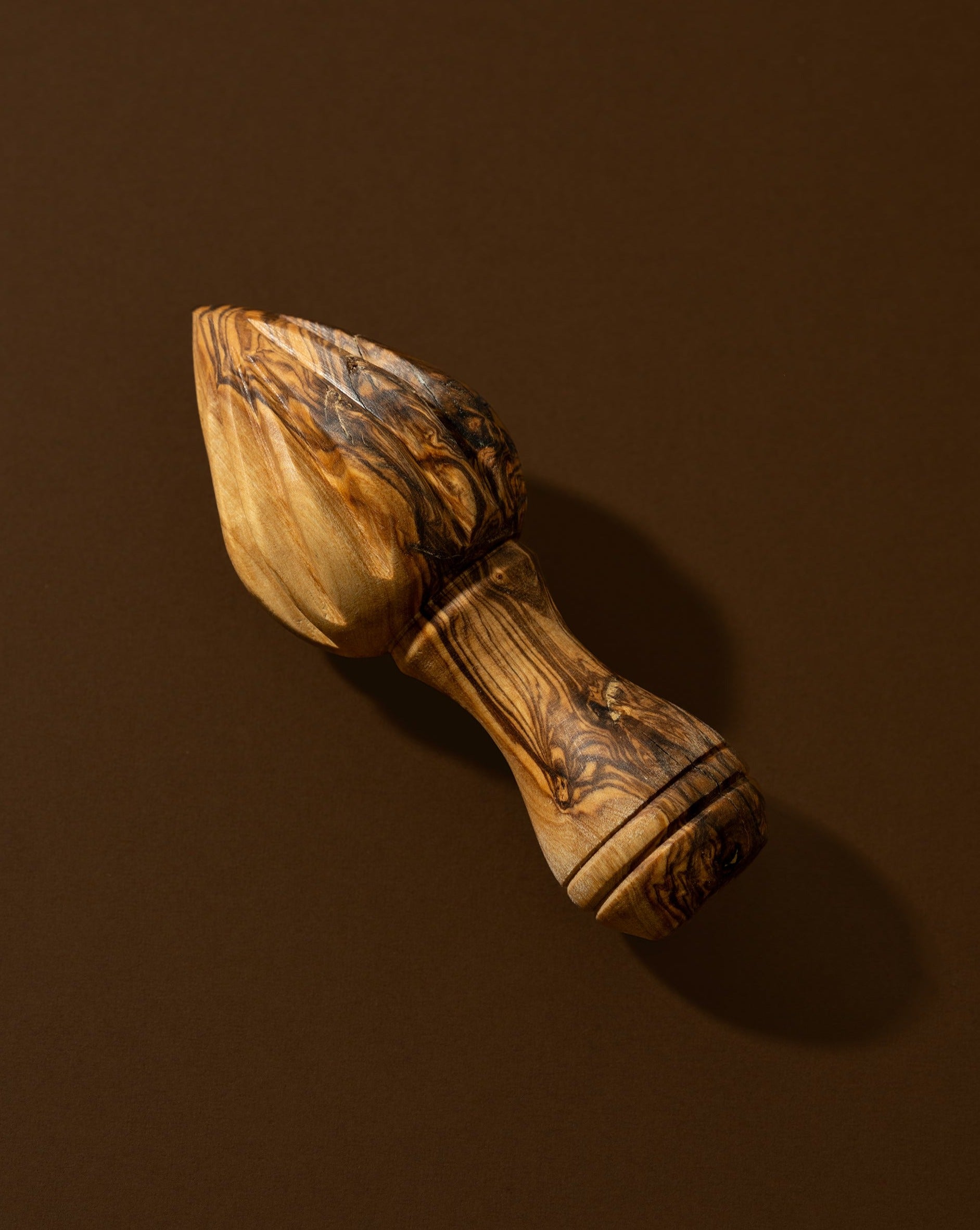 A wooden lemon press with natural olive wood patterns, lying on a brown surface. 
