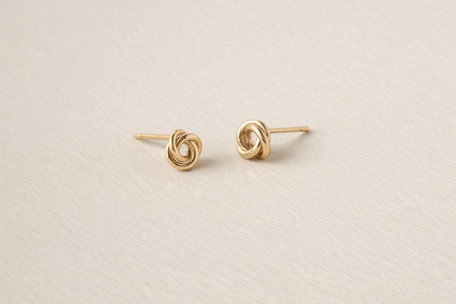 Pair of gold knot earrings on a beige background