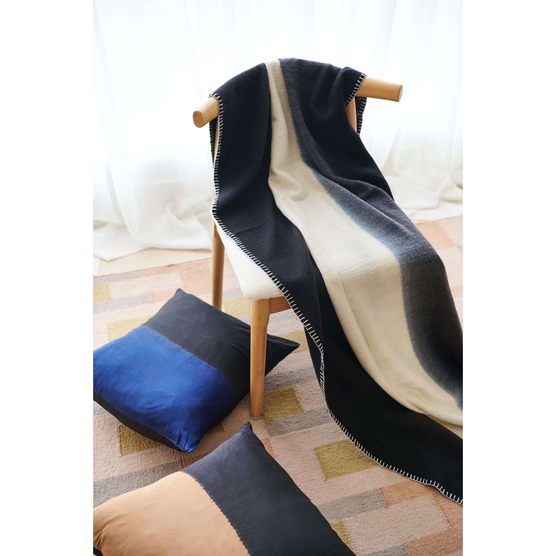 Ink Black White Ombre Textured Throw In Hand Spun Merino And Hand Stitched Hem draped over a chair with pillows.