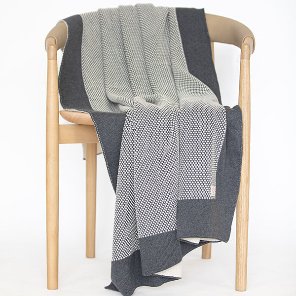 Gray and black patterned throw blanket draped over a wooden chair on a white background.