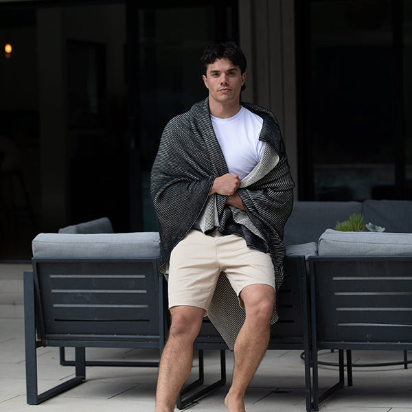 Man sitting on outdoor furniture with a black ribbed organic cotton blanket draped over his shoulders.