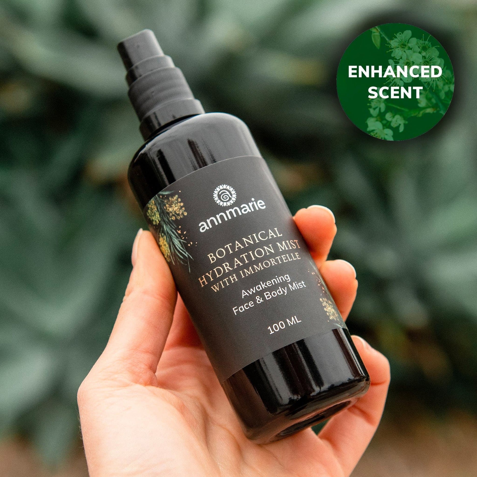 Hand holding a black bottle of 'annmarie' botanical hydration mist with greenery in the background
