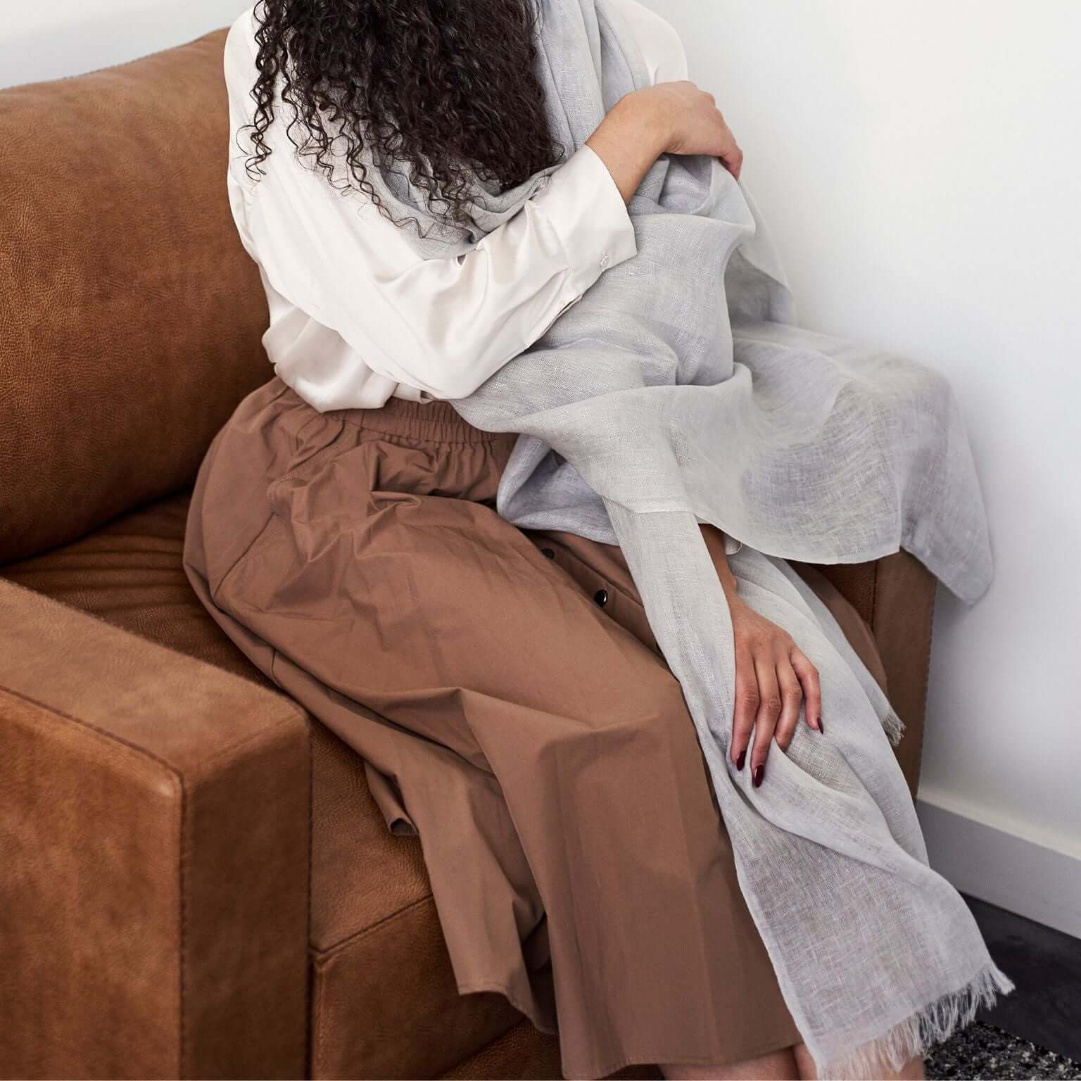 Pebble Light Gray Hand Woven Soft Linen Scarf draped elegantly over a person sitting on a brown couch.