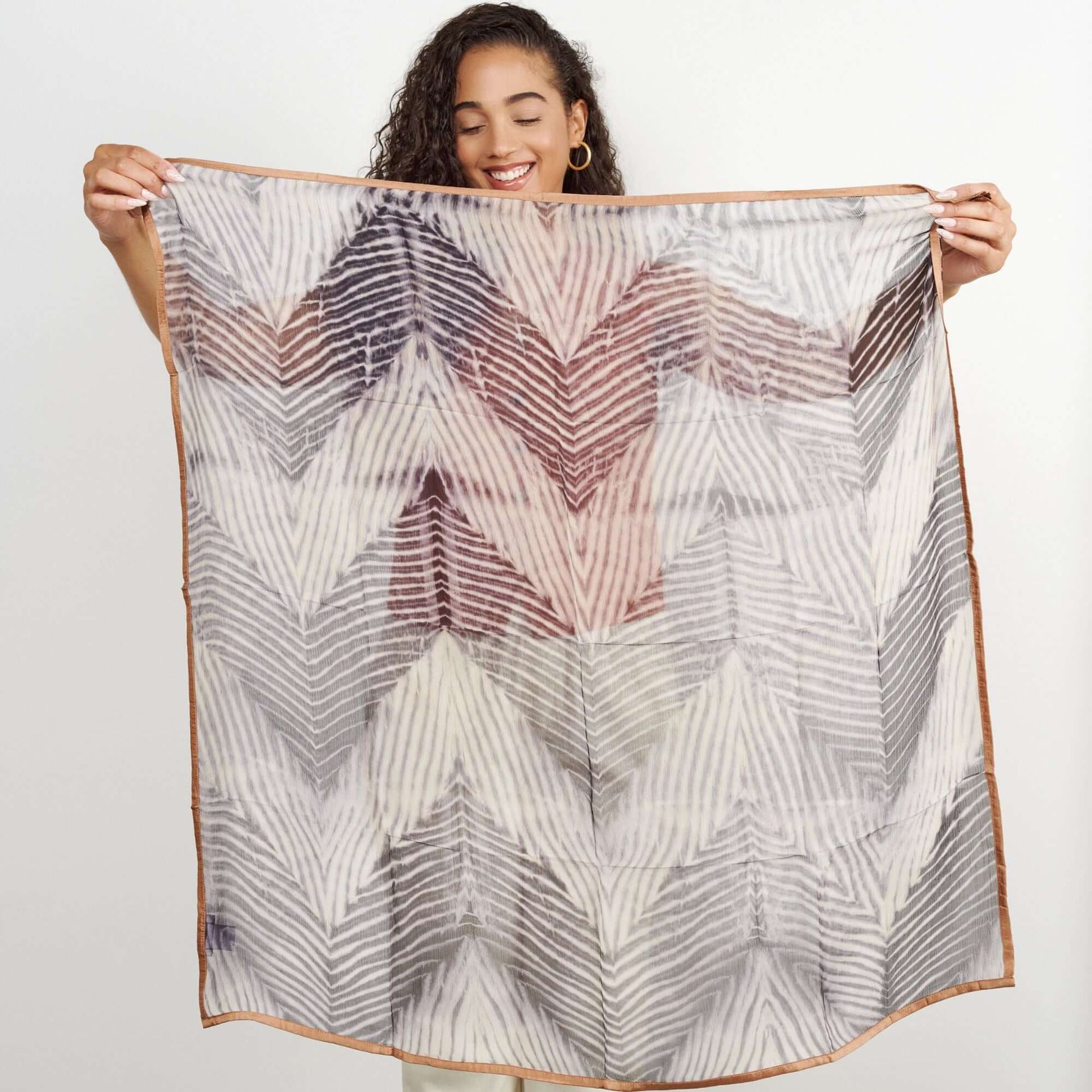 Woman holding a Samu Black hand crafted chiffon square scarf with a shibori print design.