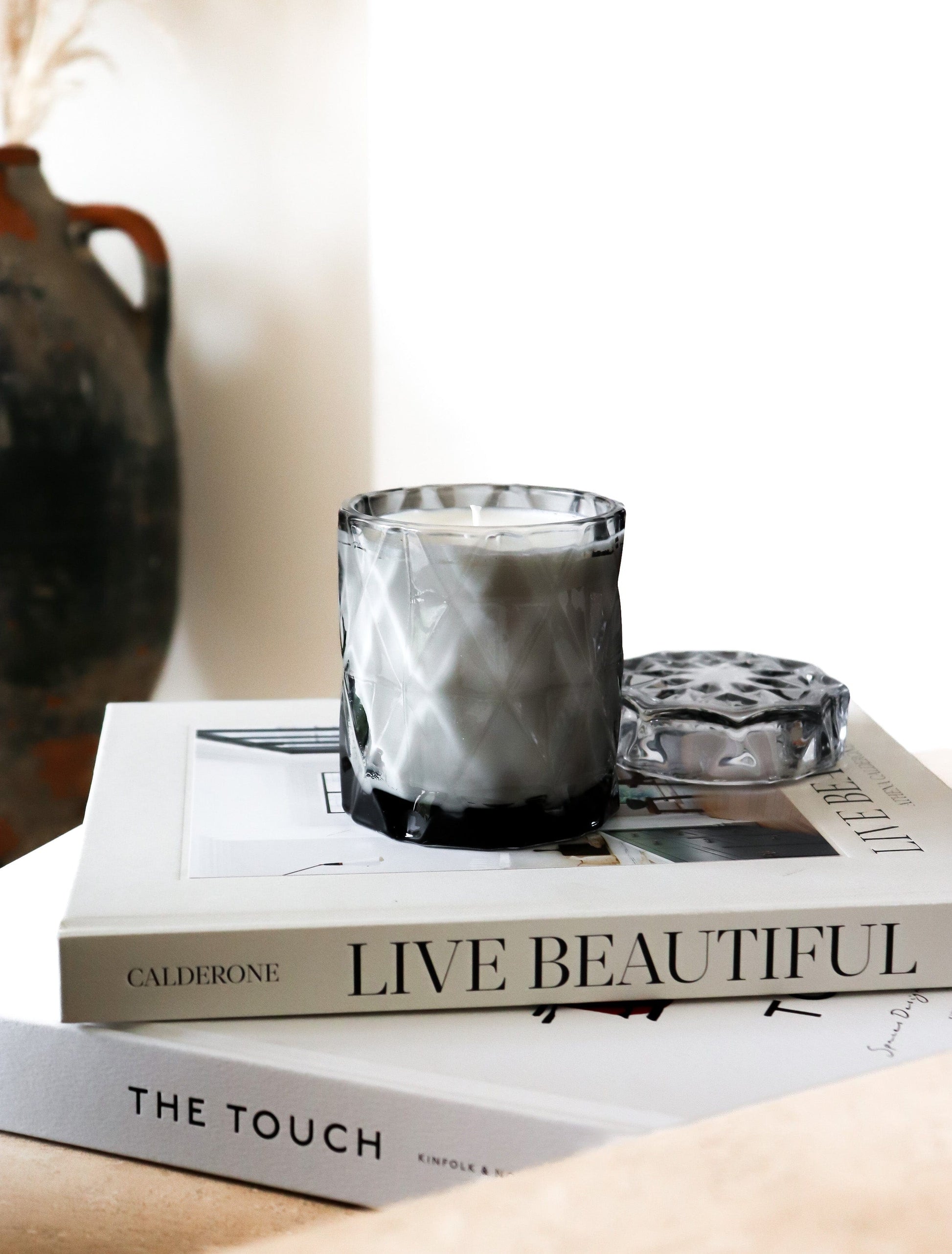coconut wax candles in a gray glass jar with lid on stacked coffee table books