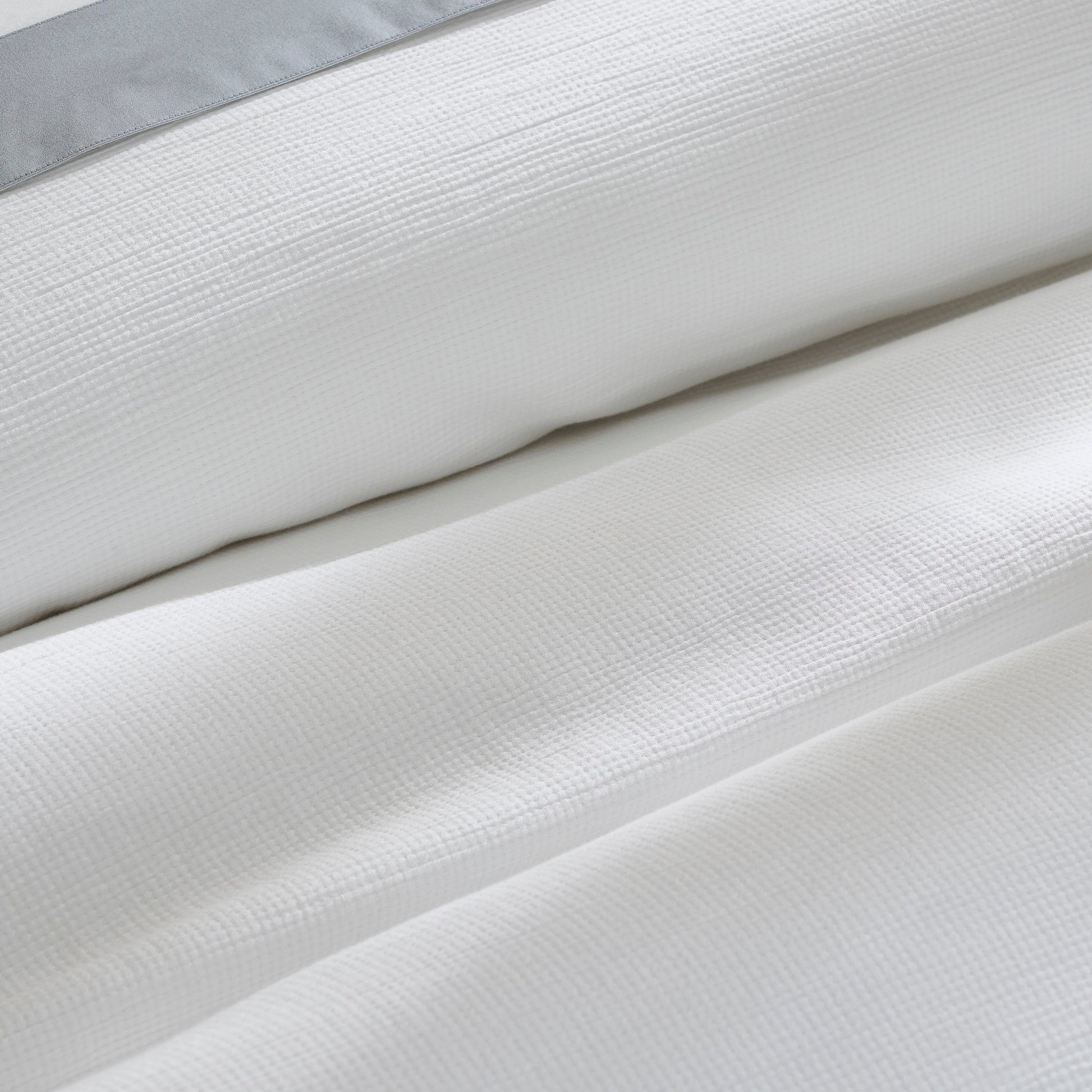 DT-067-9092_7|Close-up of a white textured duvet cover, elegantly folded with a subtle grey accent, emphasizing luxurious, soft fabric.