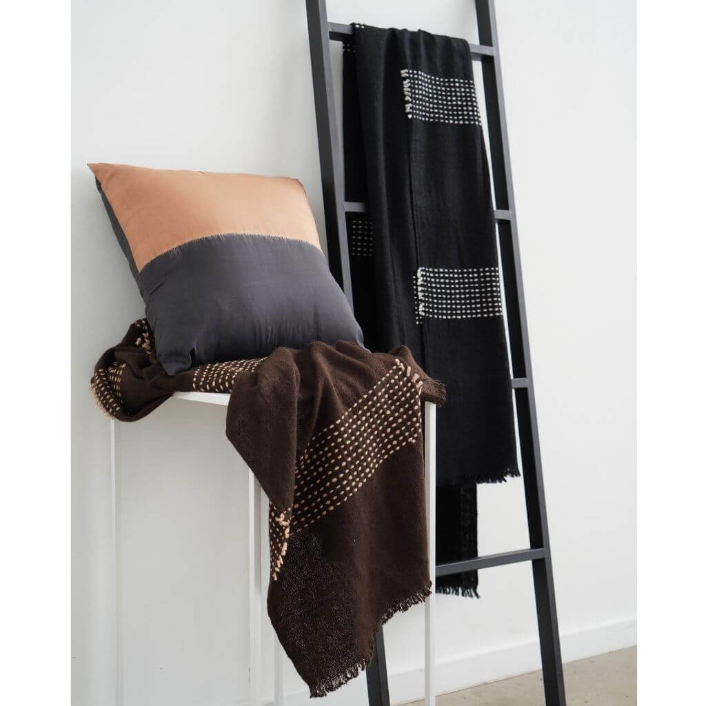 Walnut Black Yak With Hand Knotted Merino Stripes Handloom Throw displayed on a ladder with coordinating cushions.