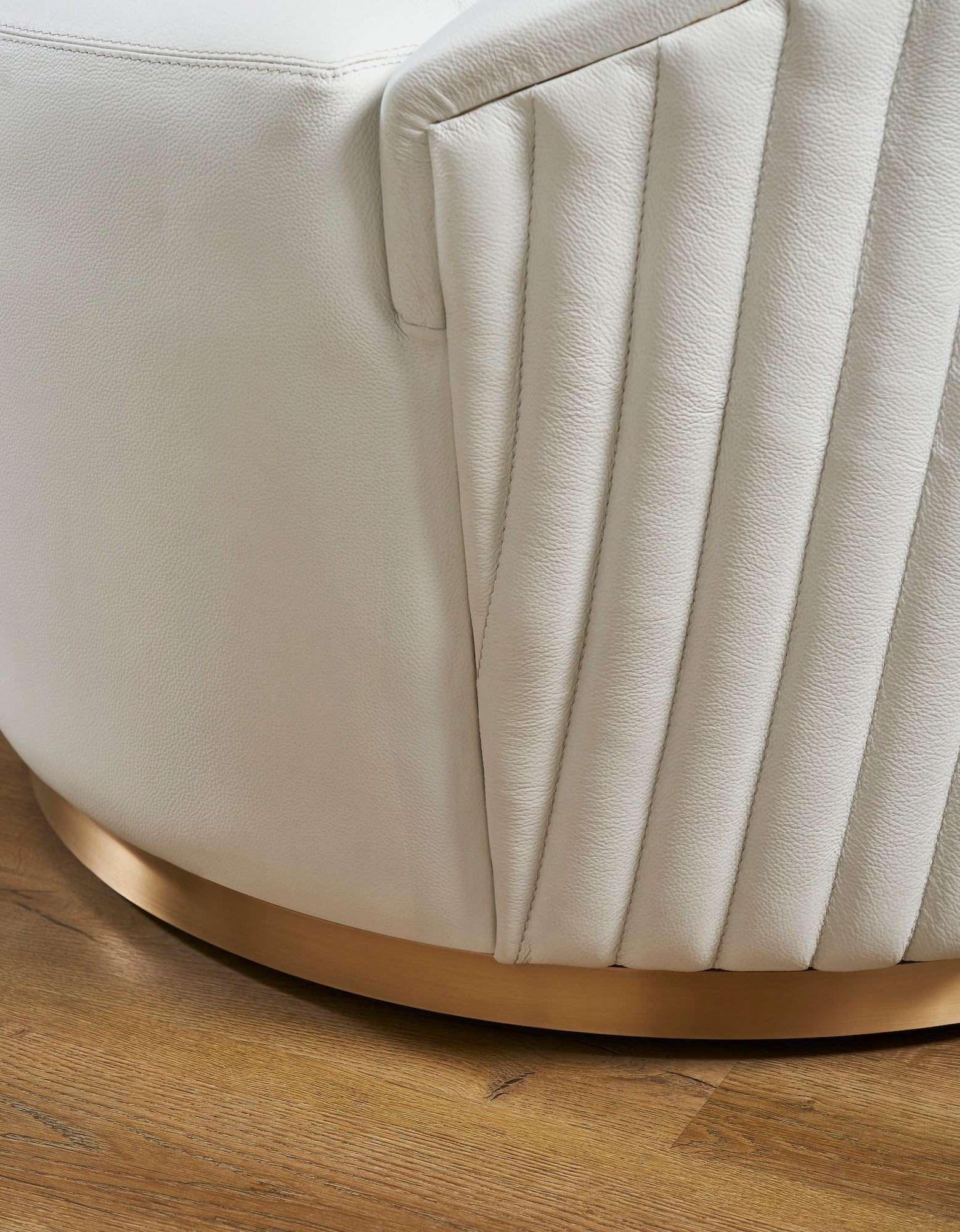 FN-5206-353529_7|Detailed view of white leather swivel armchair's vertical ribbed texture and gleaming gold metal base, emphasizing luxurious design.