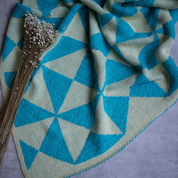 Organic cotton throw with aqua blue geometric wind mill patterns next to dried white flowers.