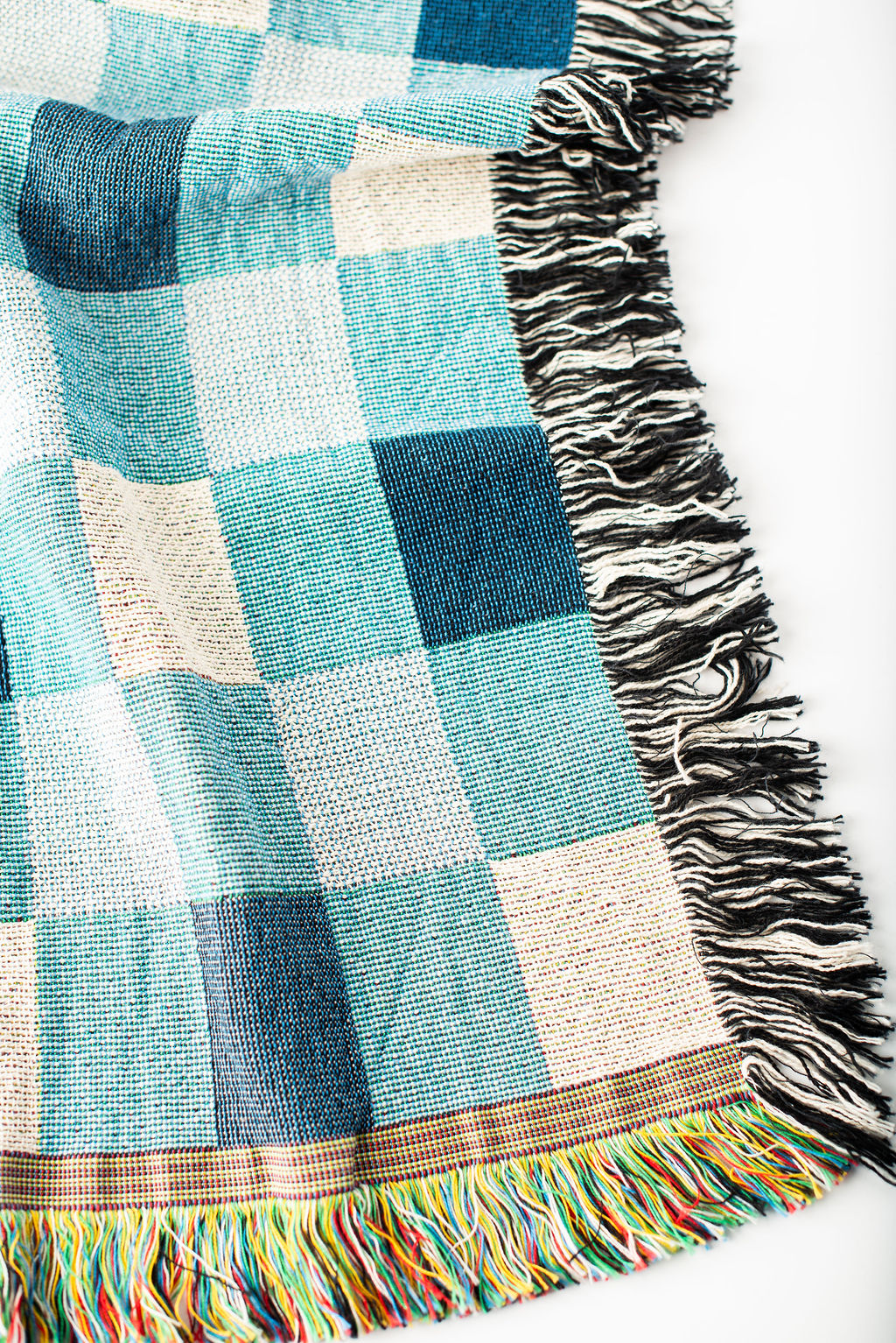 Close-up of Tilda Bayberry blue, aqua, and cream check woven cotton throw with fringe