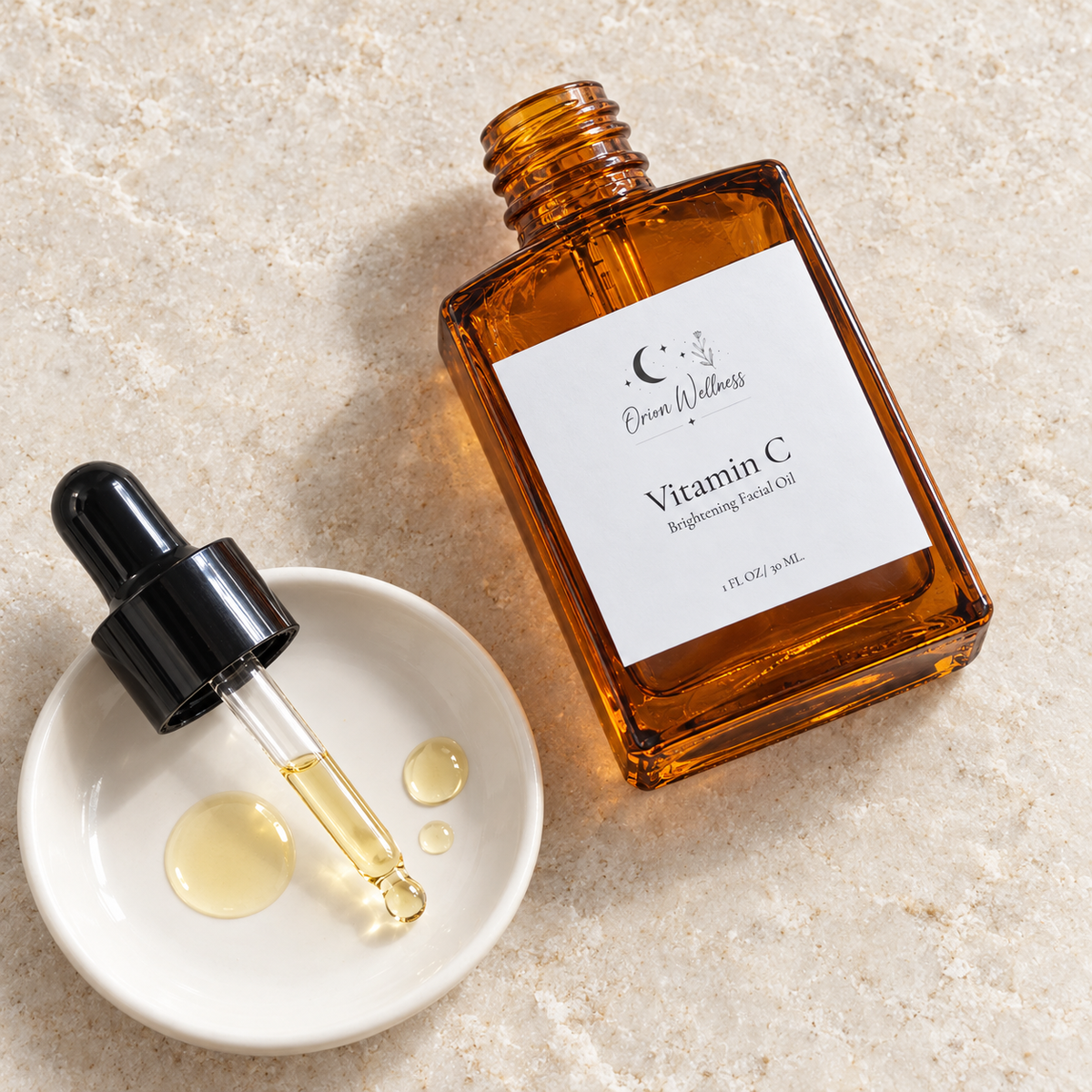 Vitamin C Brightening Facial Oil bottle and glass dropper beside golden oil drops on a white ceramic dish