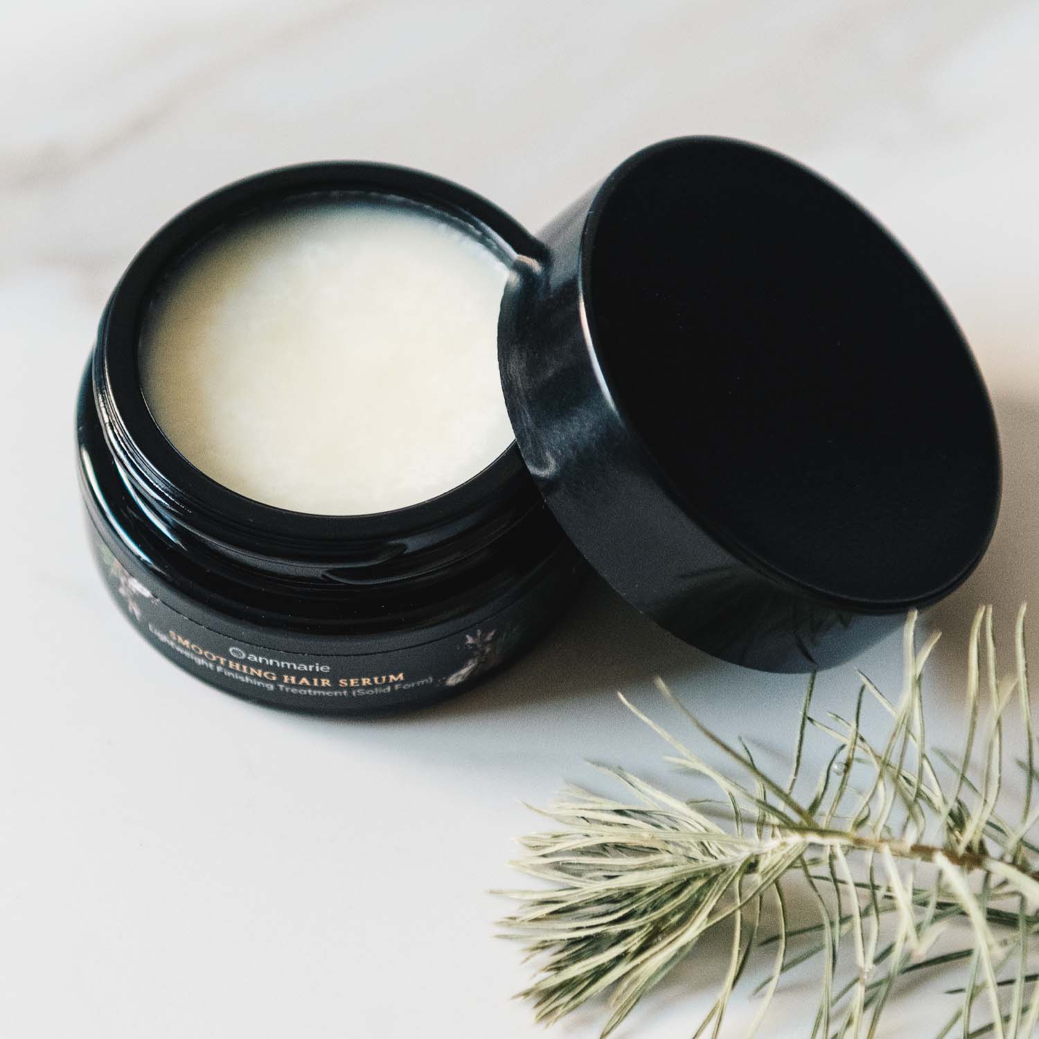 Smoothing Hair Serum in solid form with the lid beside it, showing the smooth balm texture inside