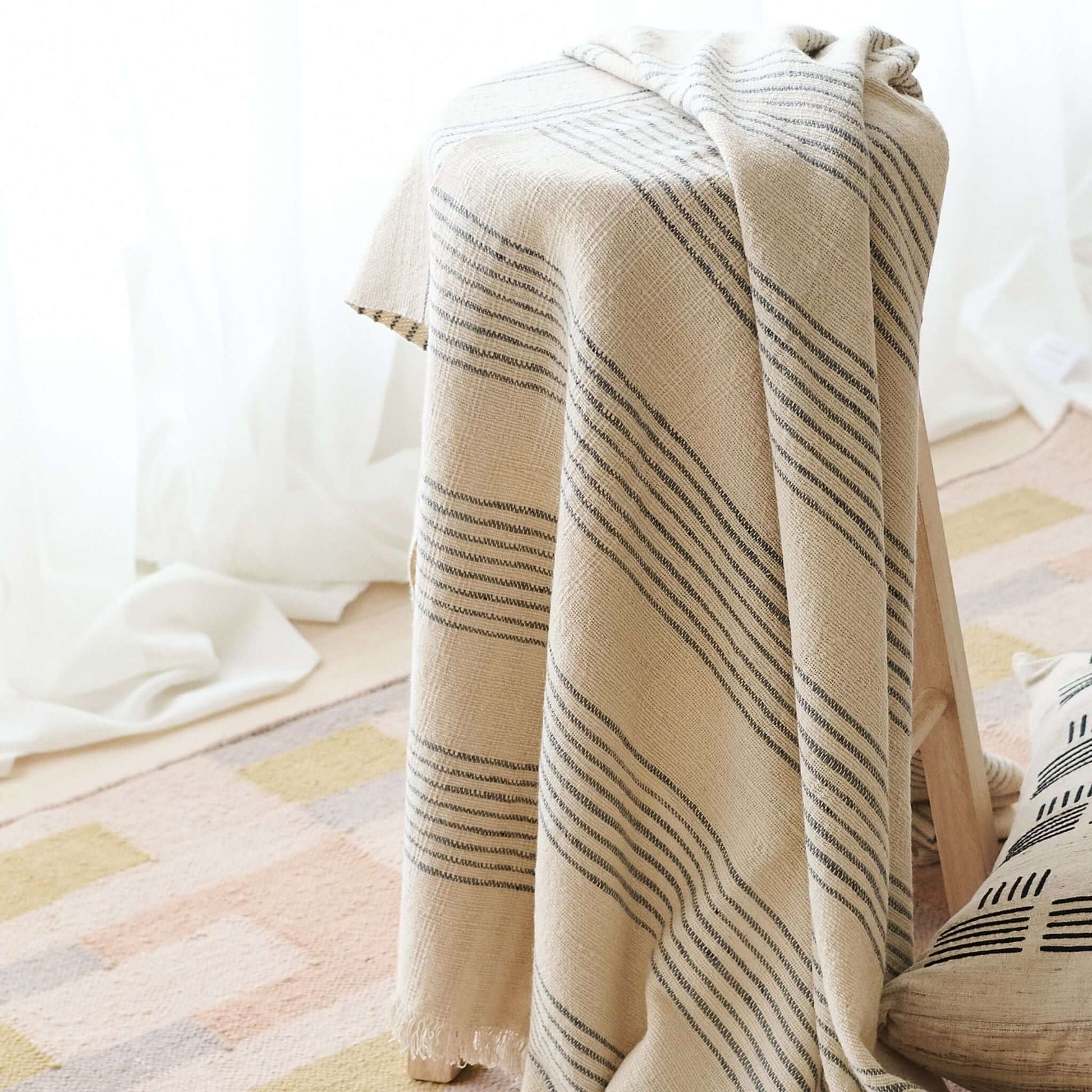 Silica Chalk Off White And Gray Stripes Pattern Soft Handwoven Merino Throw draped over a chair in a cozy setting.