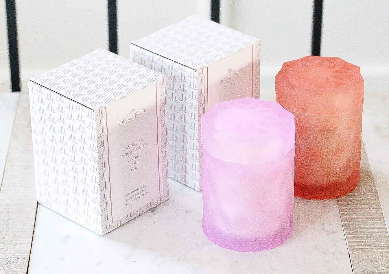 lavender lilac color and coral color glass candle jars with lids next to candle packaging 