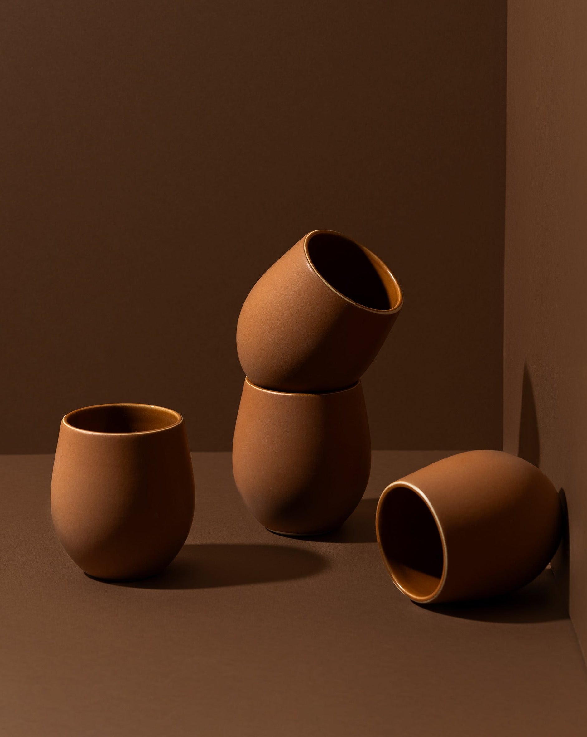 A set of four stoneware coffee cups arranged in a casual manner, with a matte terracotta finish.