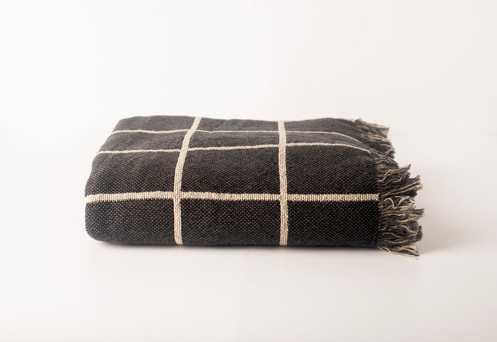Folded charcoal and cream reversible grid throw blanket with fringe