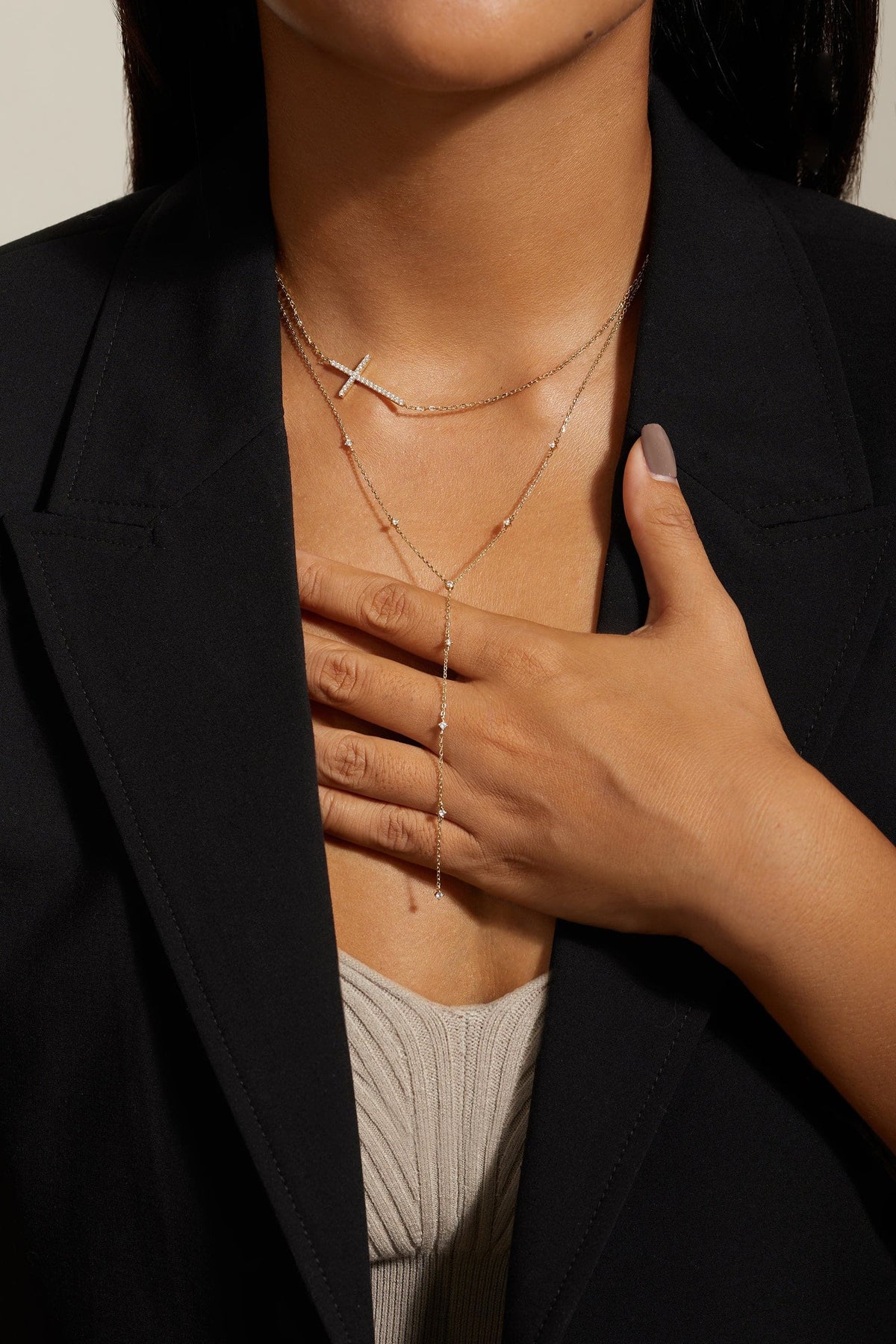 Gold-toned layered cross pendant and beaded lariat necklace worn by a person