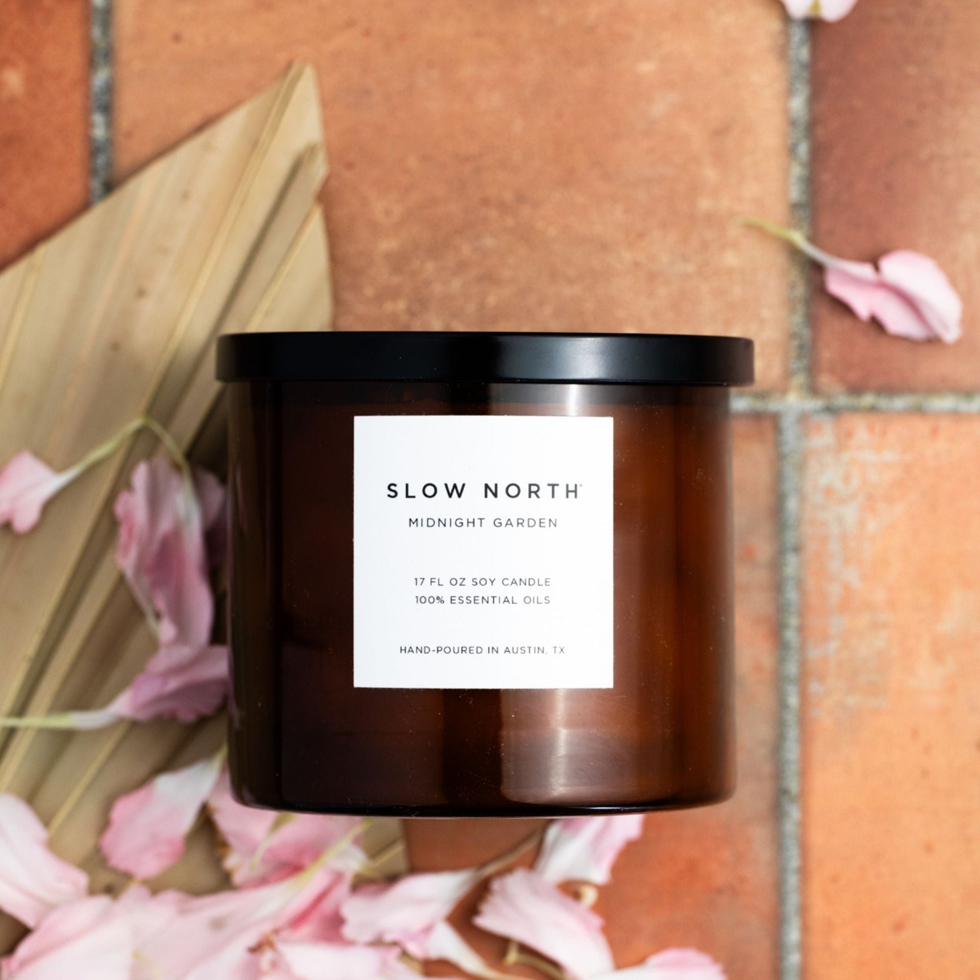 Brown candle with a white label on a brick surface with pink flowers